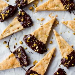 overhead image of pistachio shortbread triangles with the ends dunked into dark chocolate and sprinkled with sea salt and crushed pistachios