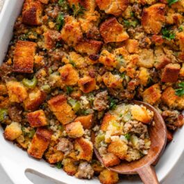 wooden spoon scooping out cornbread stuffing from white dish.