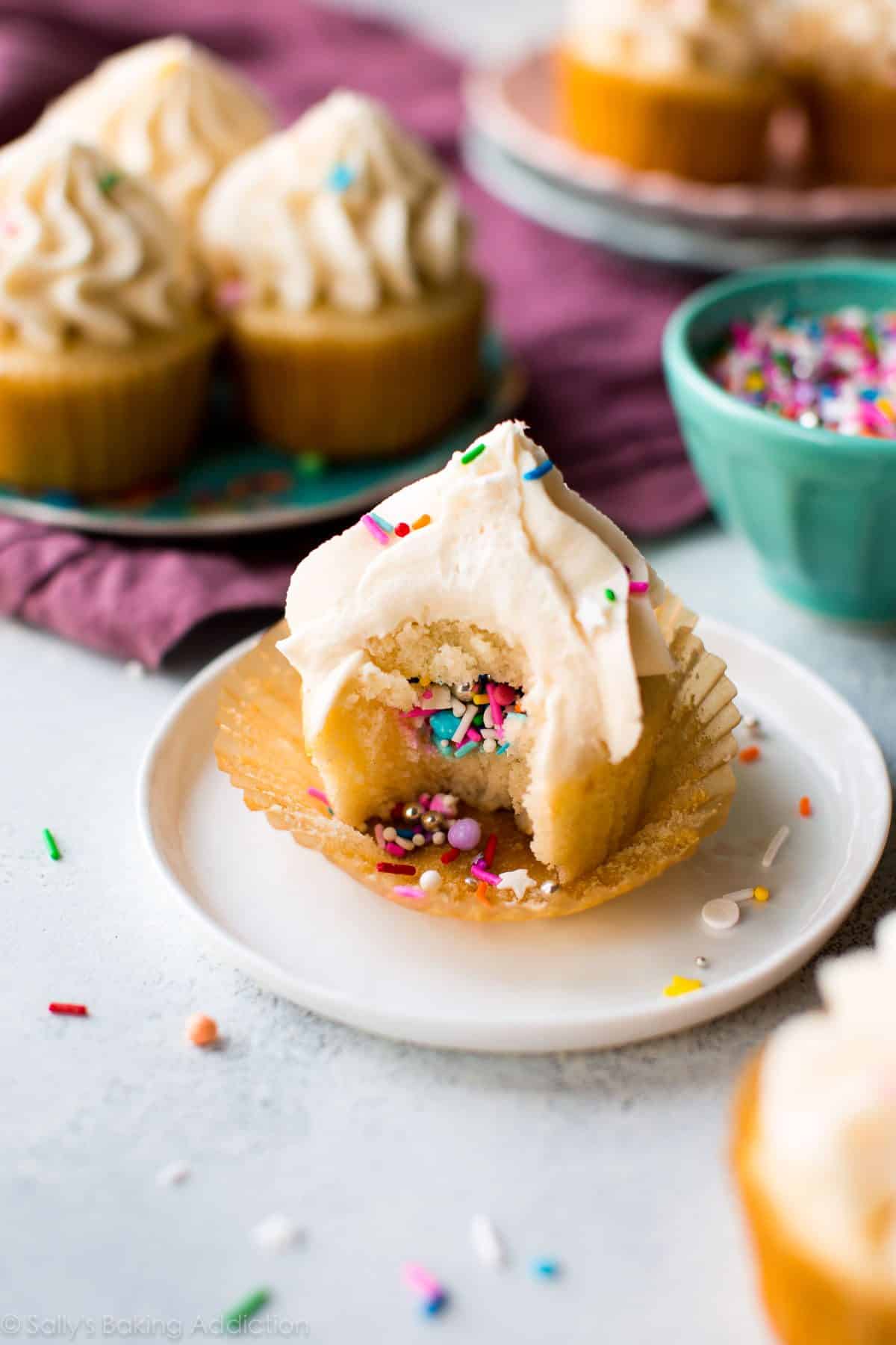 piñata cupcake on a white plate with a bite taken from it showing the sprinkles in the middle