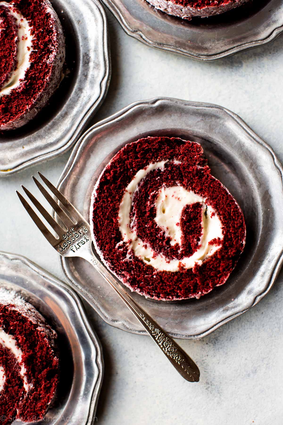 overhead image of slices of red velvet cake roll on silver plates with a fork