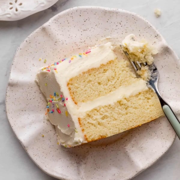 slice of white cake with forkful taken out on ruffled ceramic plate.