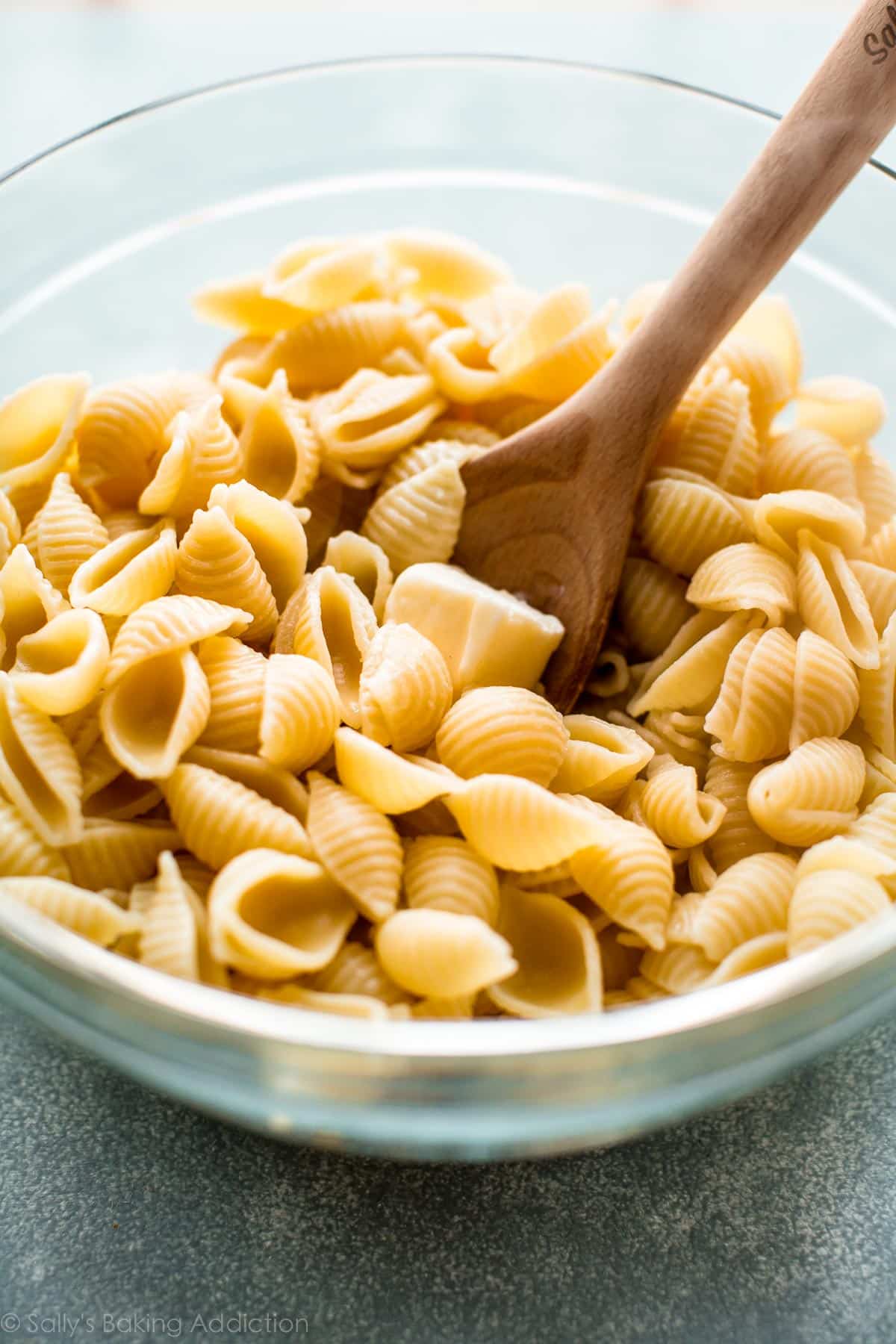 buttered noodles in a glass bowl with a wood spoon