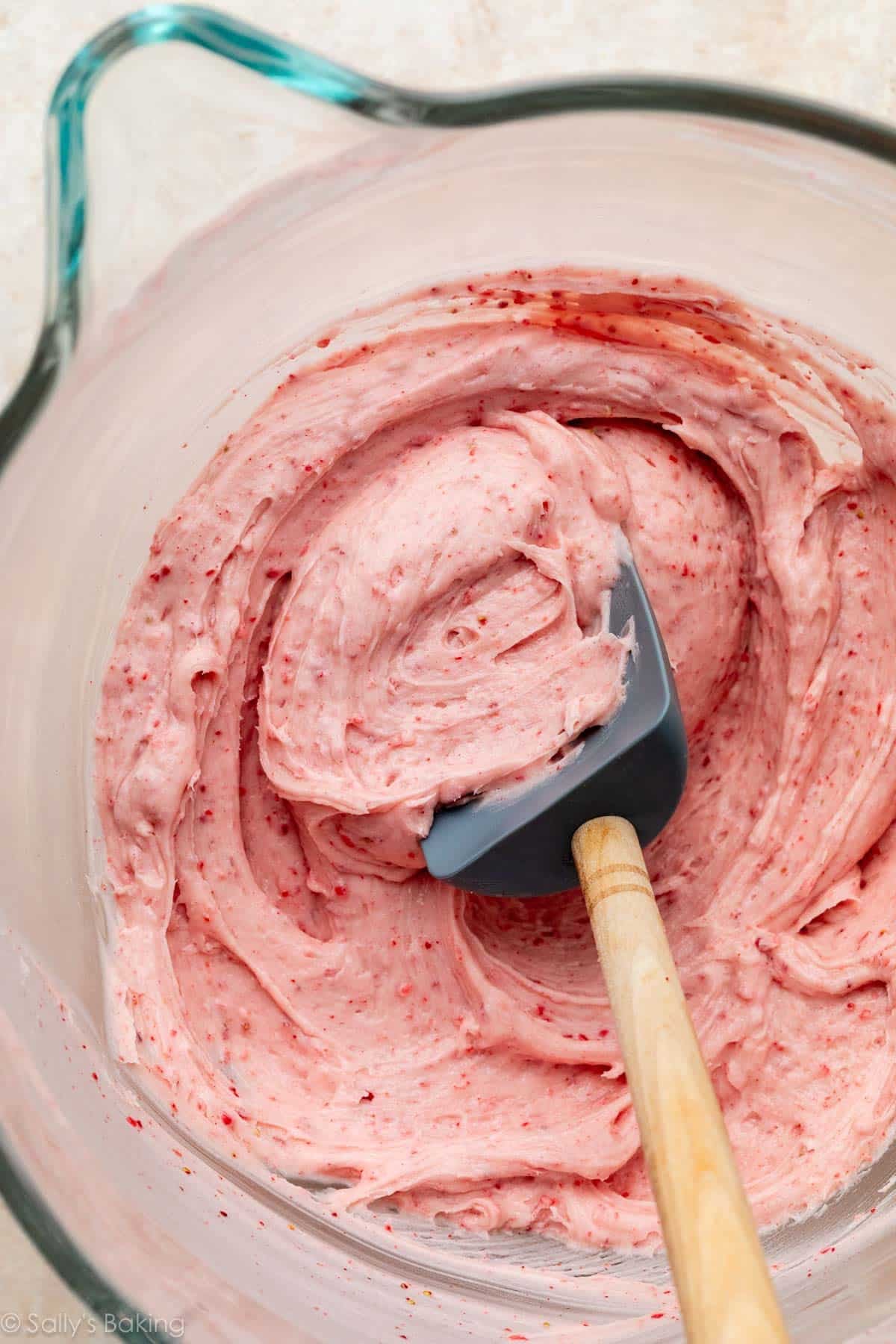 creamy strawberry buttercream in glass bowl with blue spatula.
