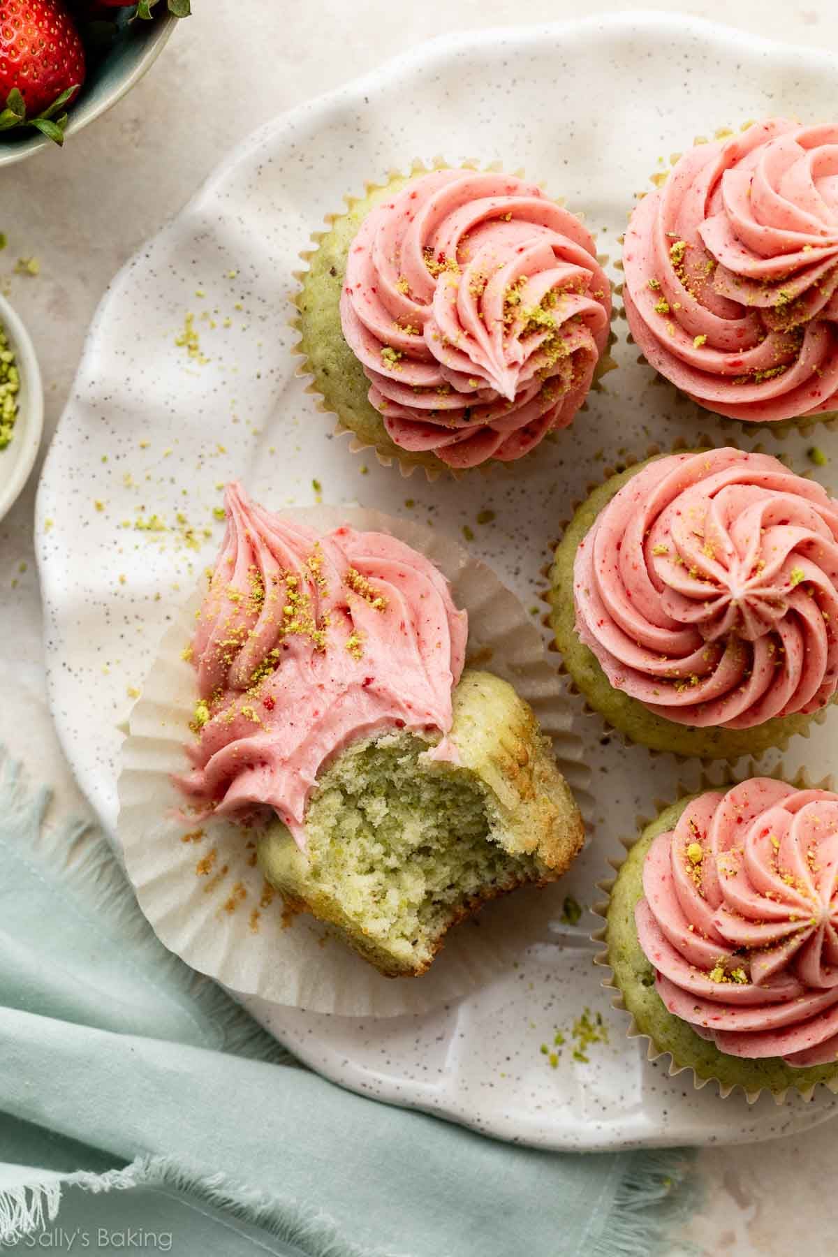pistachio cupcakes with pink strawberry buttercream frosting on top on a white plate.