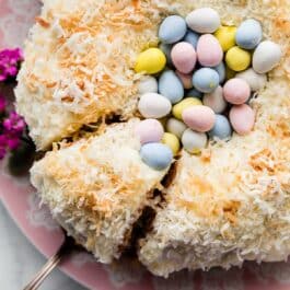 Easter cake decorated like a nest with a Bundt cake, coconut, and Easter chocolate egg candies on pink serving dish.