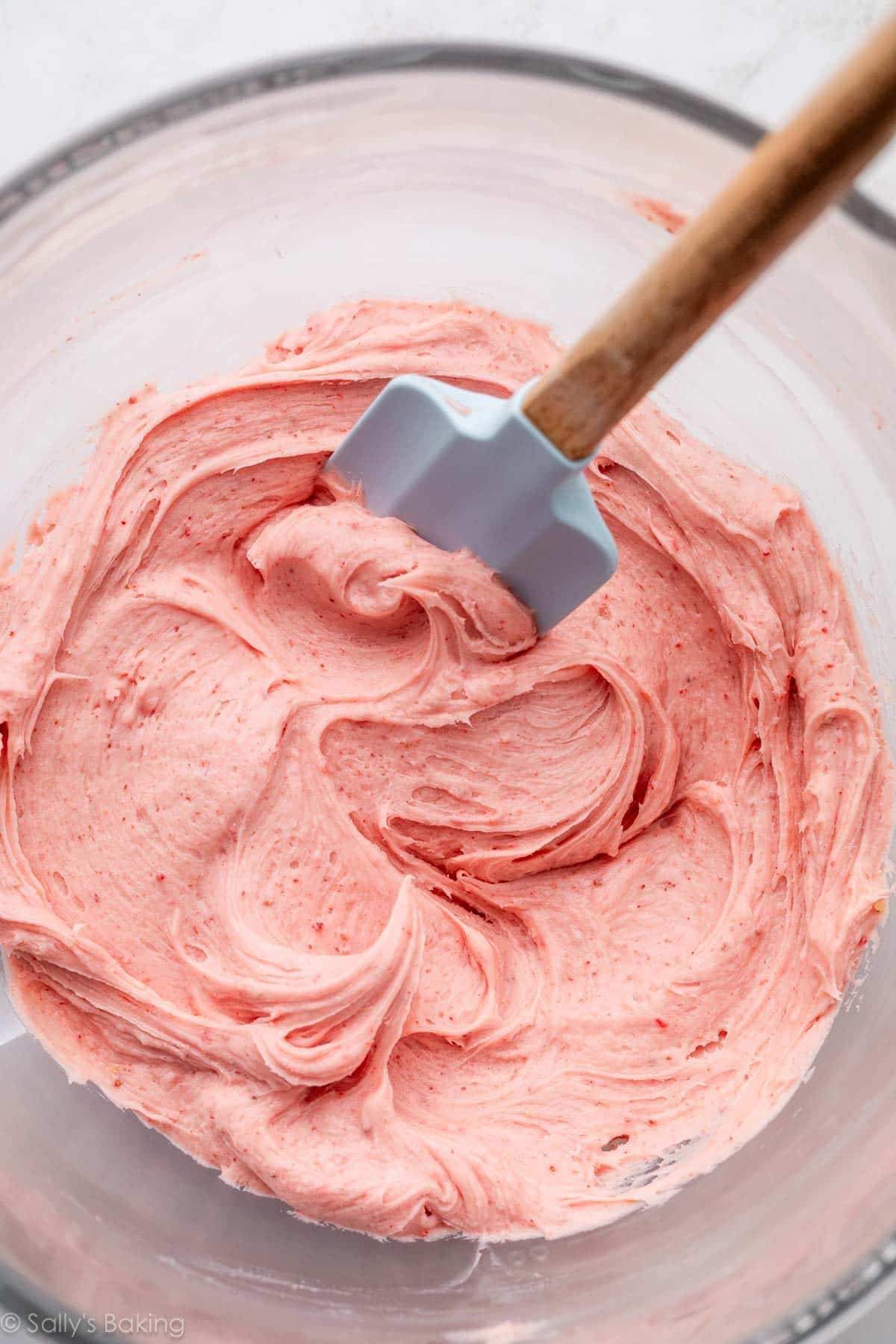 creamy strawberry buttercream in glass bowl with blue spatula.