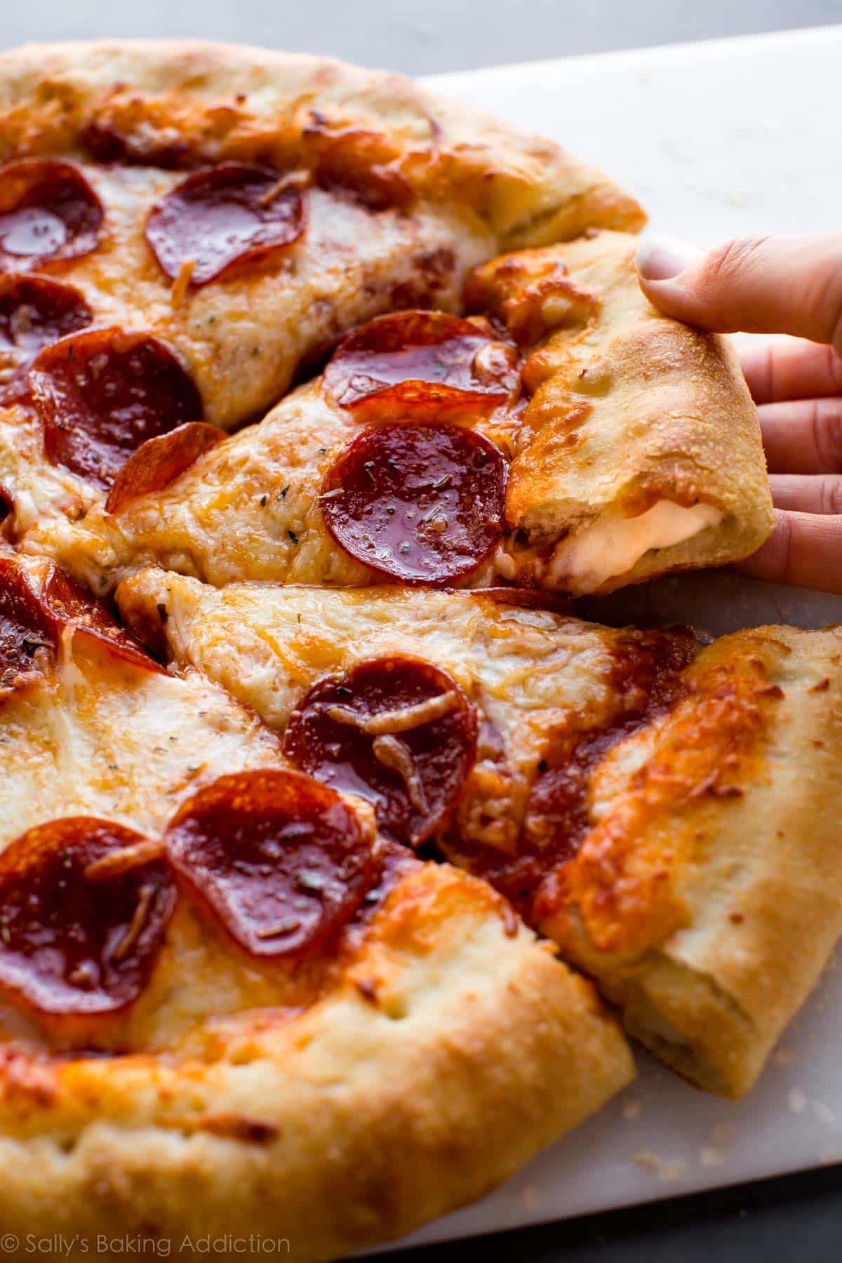 hands pulling out a slice of stuffed crust pizza
