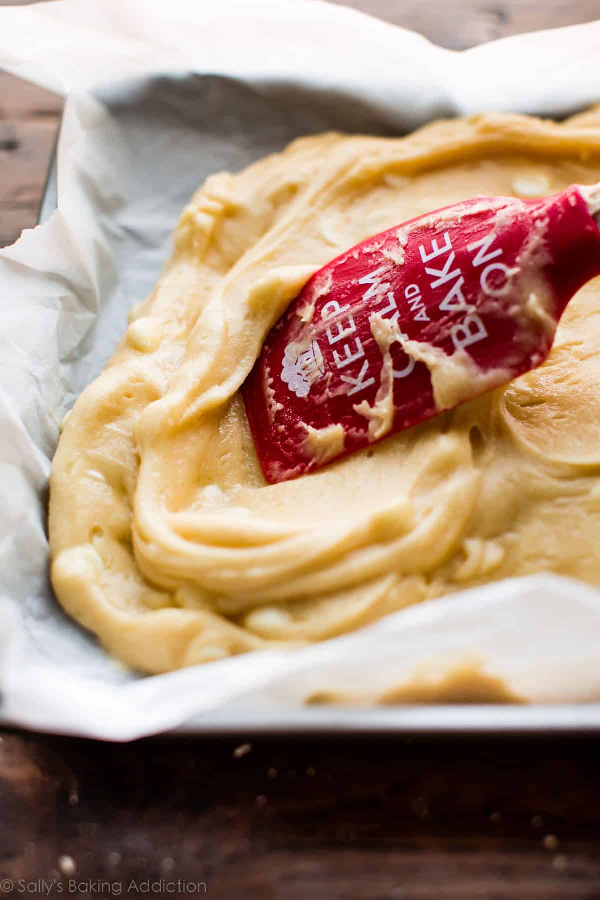 spreading white chocolate brownie batter into baking pan lined with parchment paper