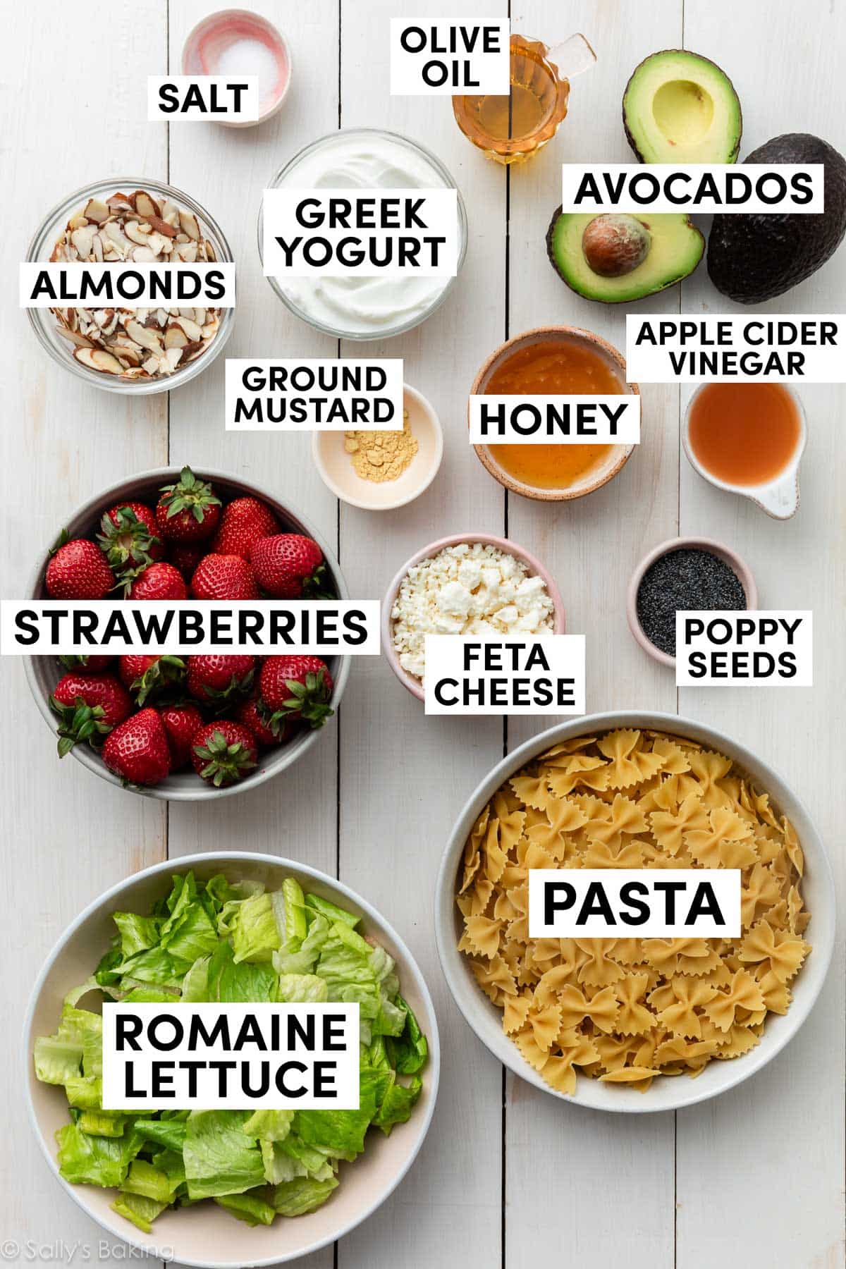 ingredients in bowls including pasta, romaine lettuce, honey, greek yogurt, almonds, avocados, and feta cheese.