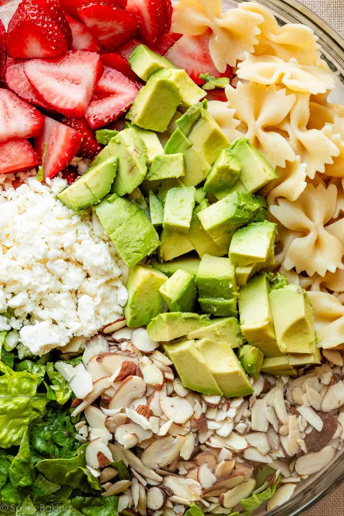 close-up of ingredients in bowl including avocado, strawberries, and sliced almonds.