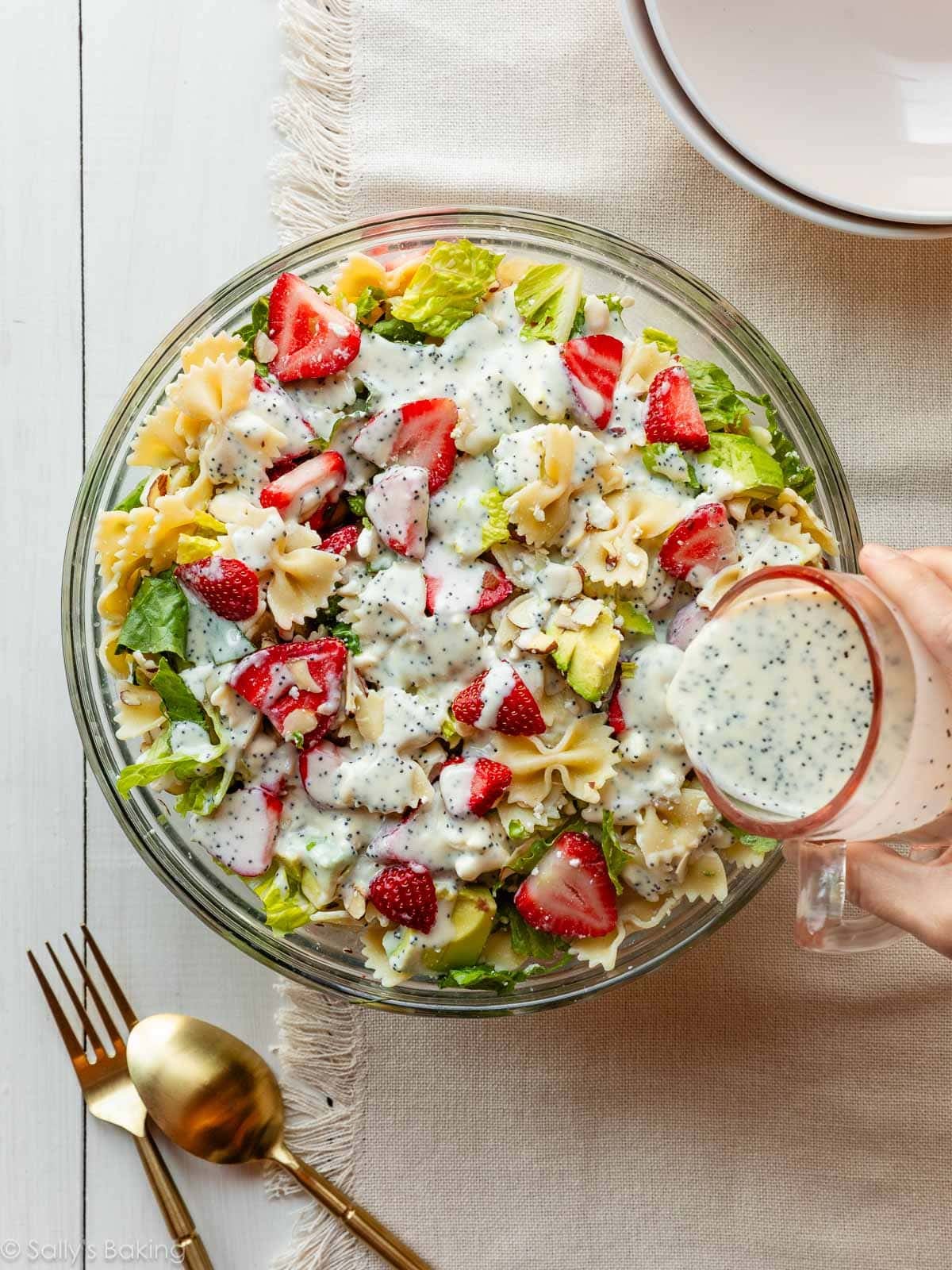pouring poppy seed dressing over ingredients in bowl.