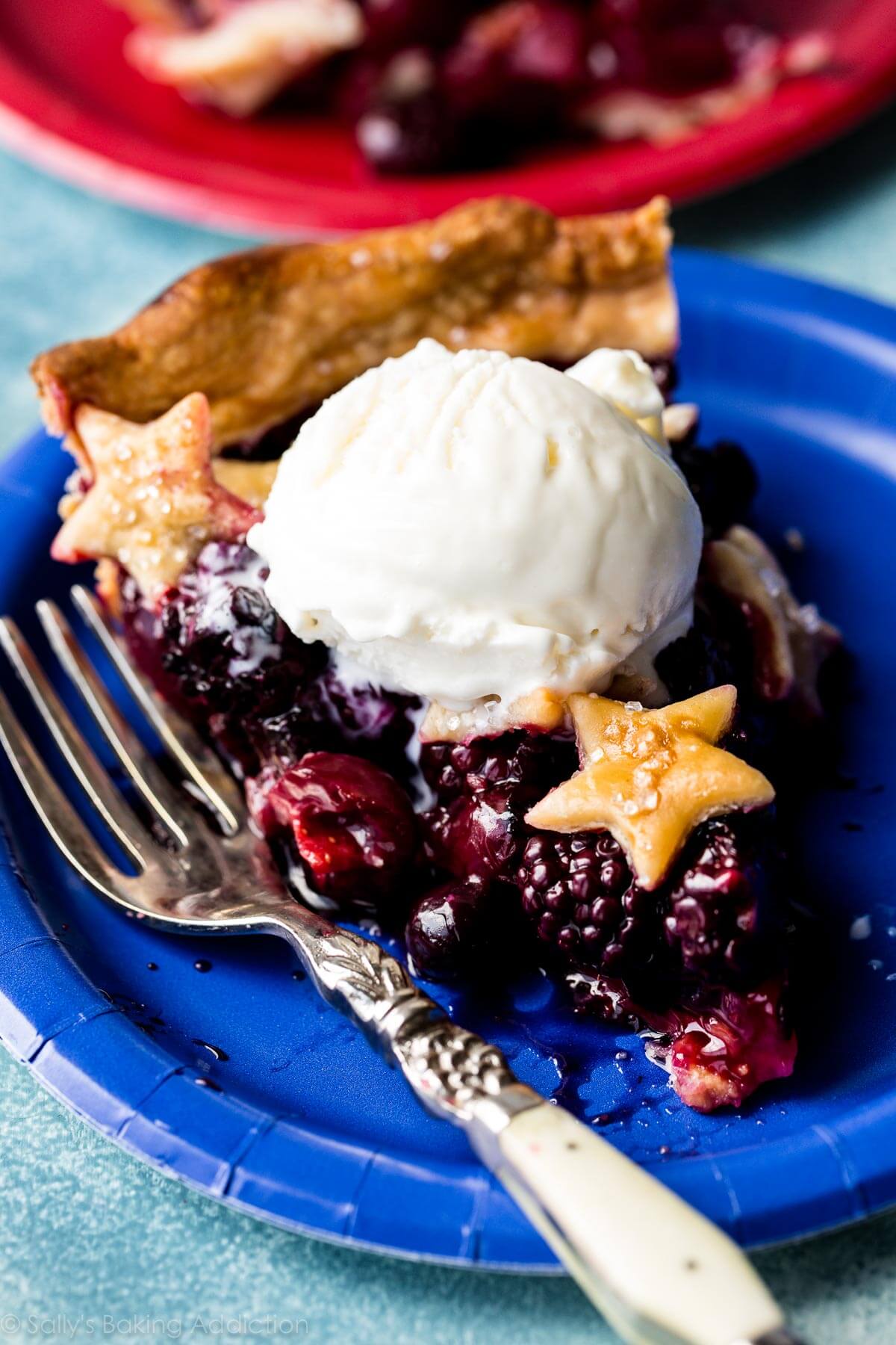 slice of American flag pie with a scoop of vanilla ice cream on a blue plate with a fork