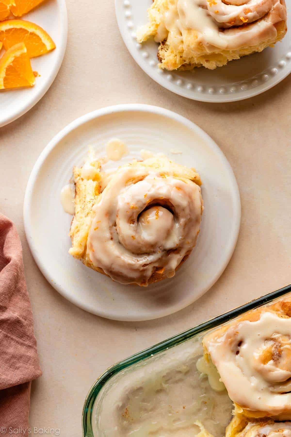 orange sweet cinnamon roll with icing on white plate.