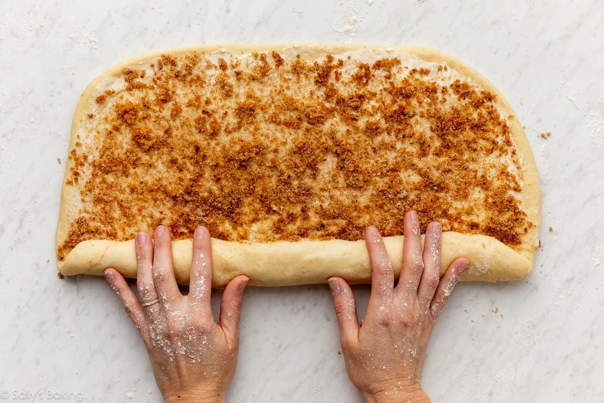 hands rolling up orange zest cinnamon roll filling.