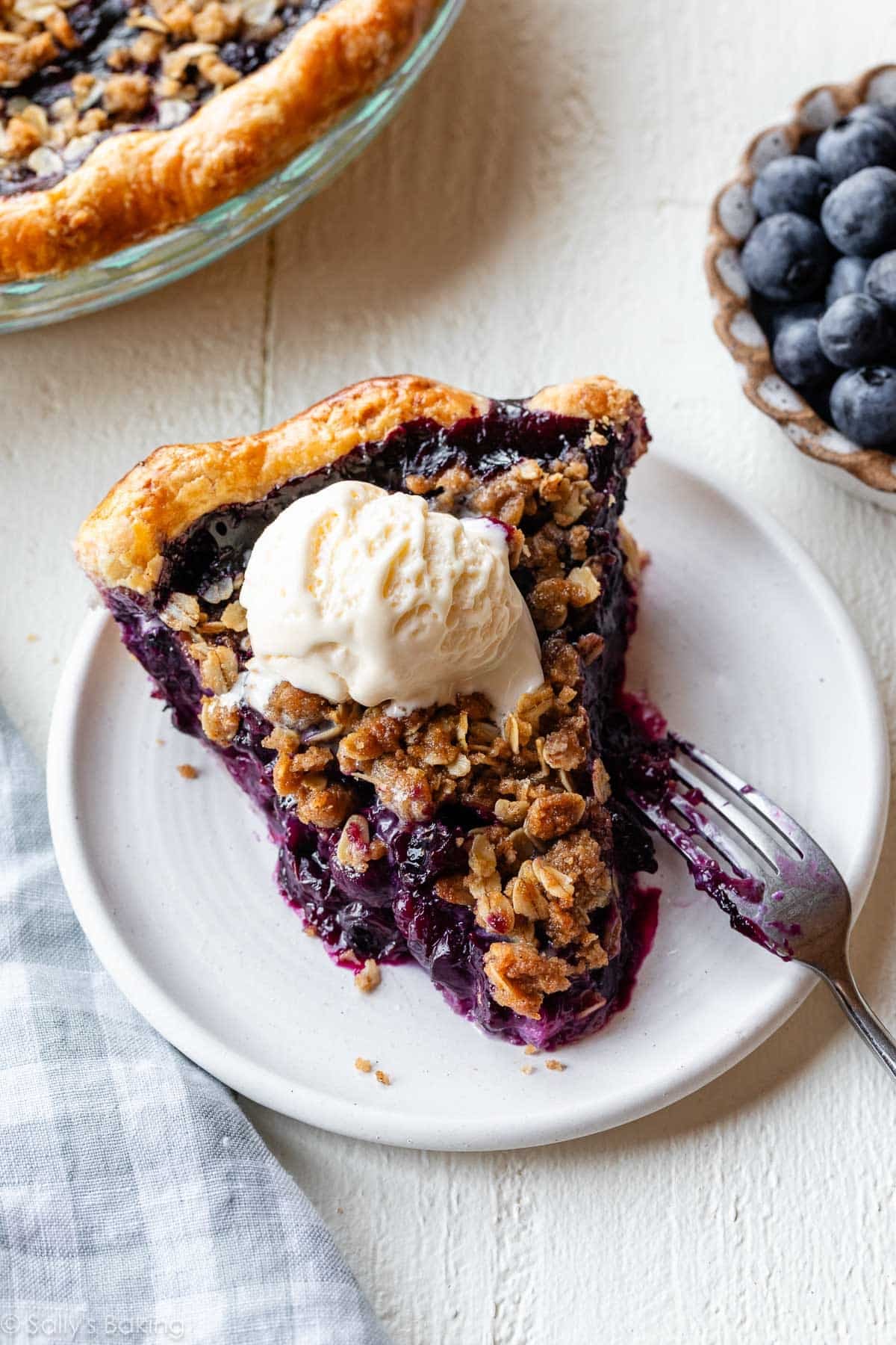 slice of blueberry crumble pie on white plate with vanilla ice cream.