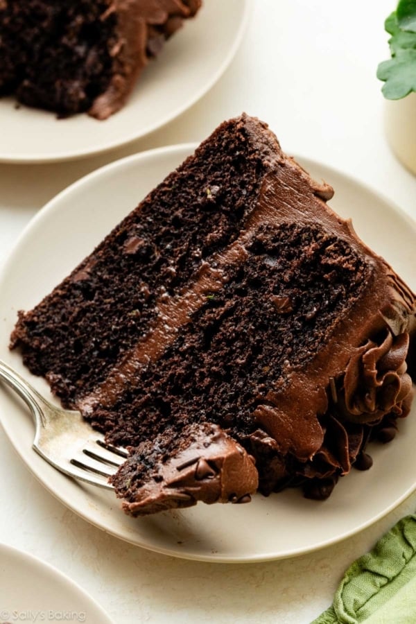 slice of chocolate zucchini cake with chocolate frosting on beige plate.