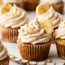 banana cupcakes with cinnamon cream cheese frosting, banana slice, and crushed nilla wafers on top.