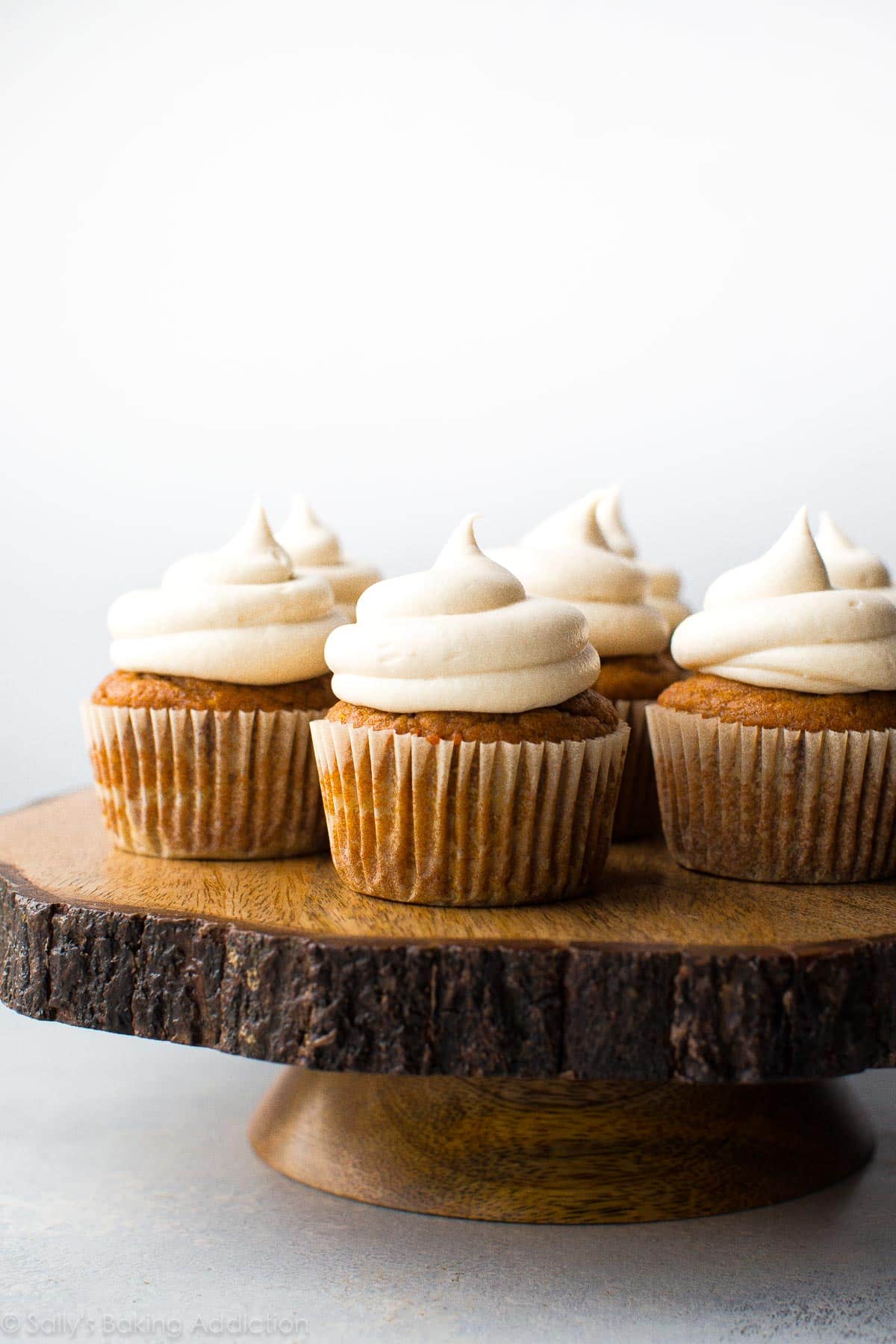 pumpkin cupcakes with cream cheese frosting on a wood slice cake stand