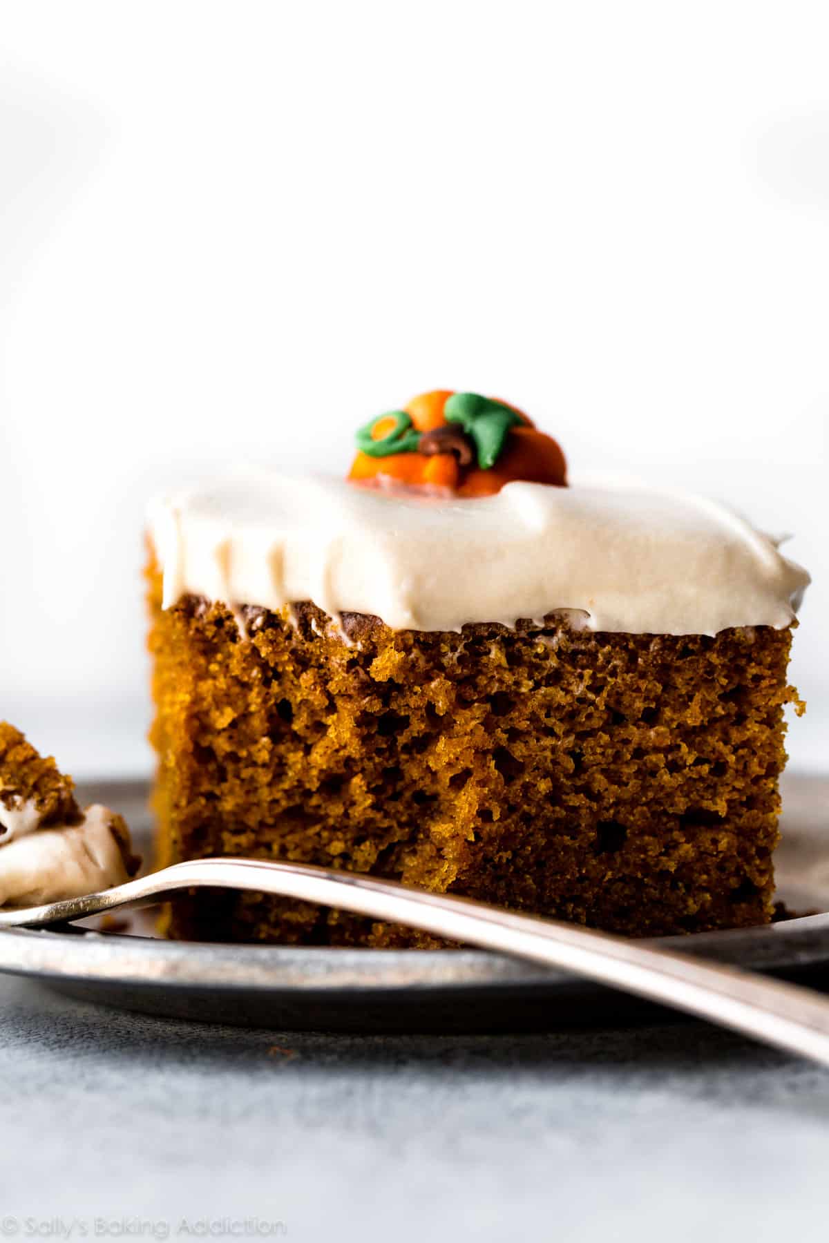 slice of pumpkin cake with cream cheese frosting on a silver plate