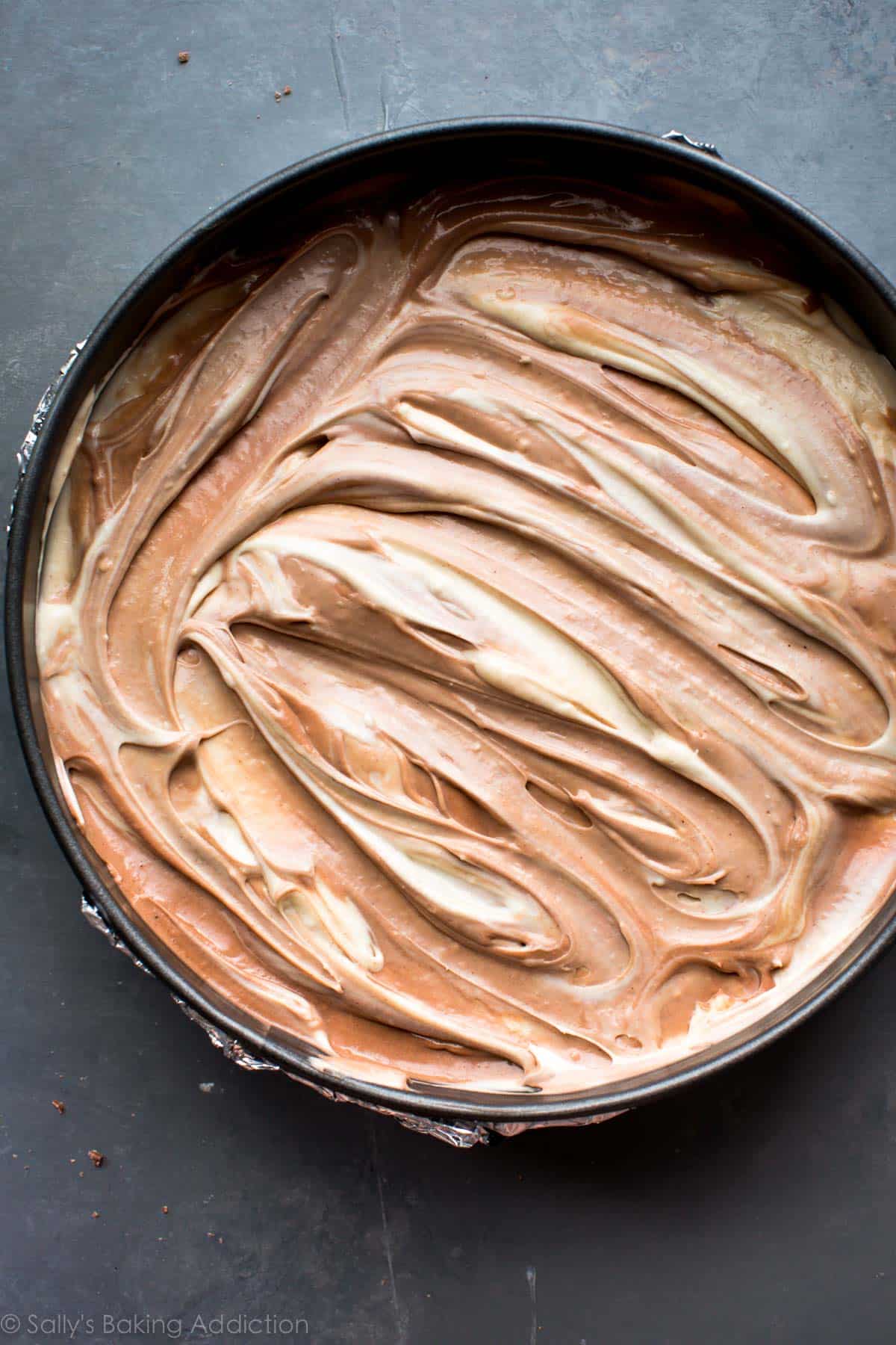 swirled chocolate and peanut butter cheesecake batters in a springform pan