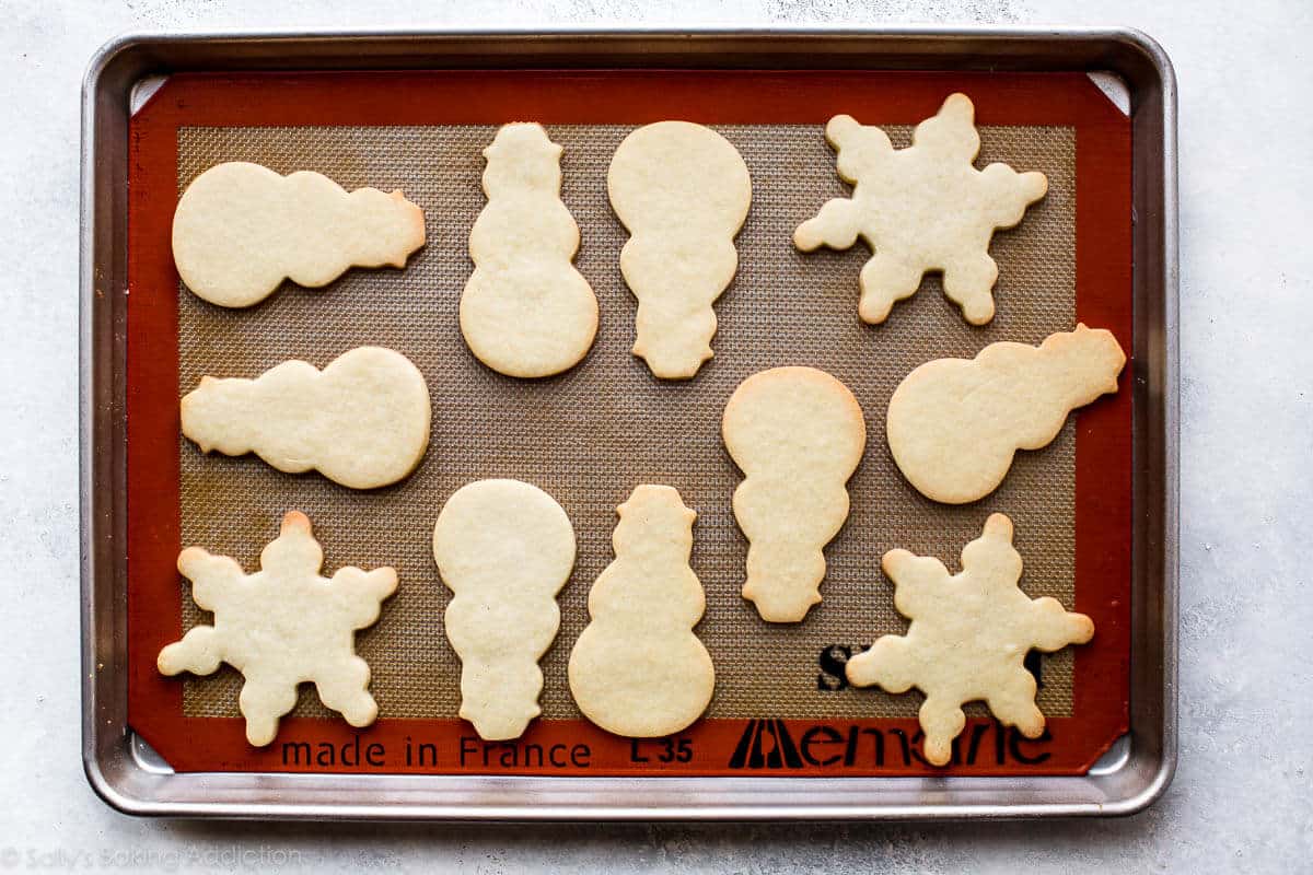 snowman and snowflake sugar cookies on a baking sheet