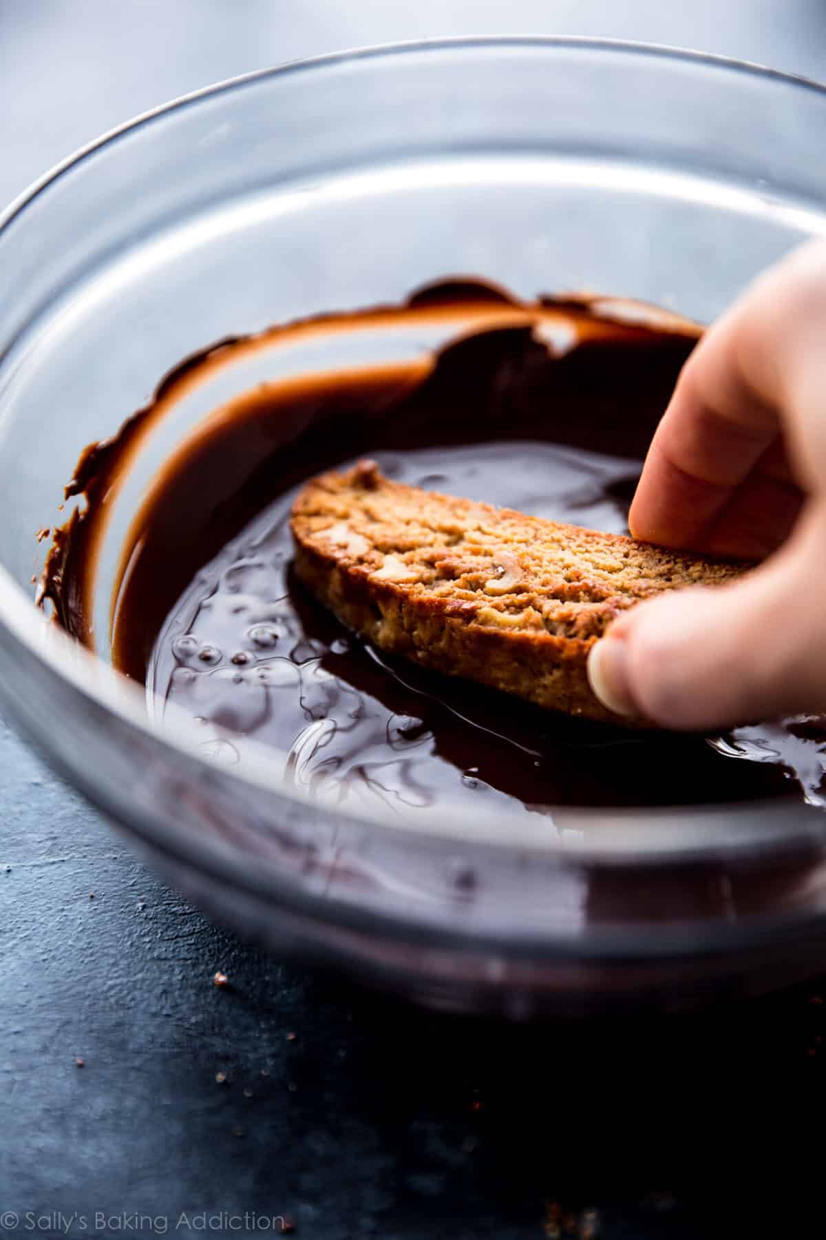 dunking orange biscotti into a bowl of dark chocolate