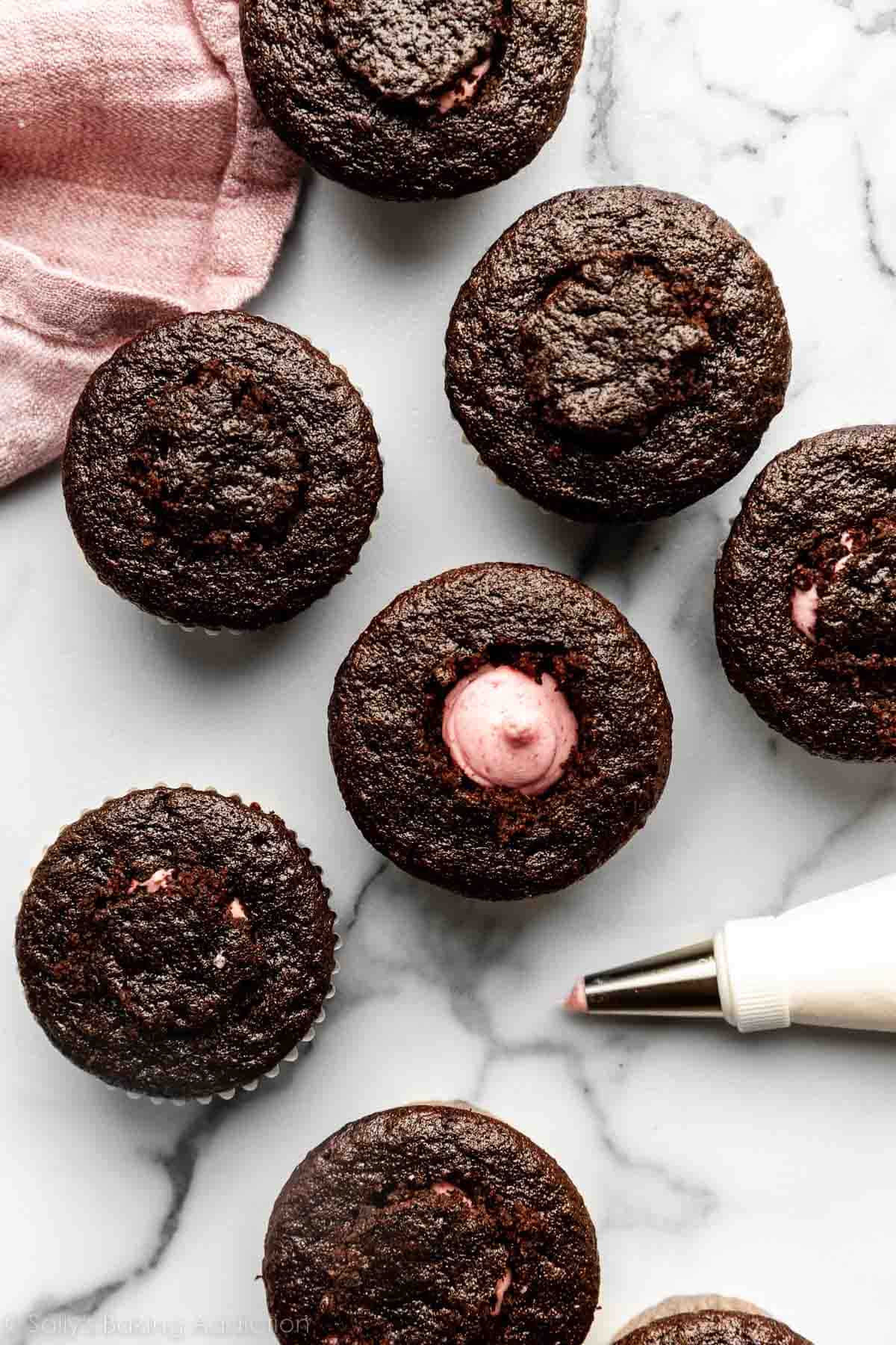 chocolate cupcakes on marble counter with one filled with strawberry buttercream.