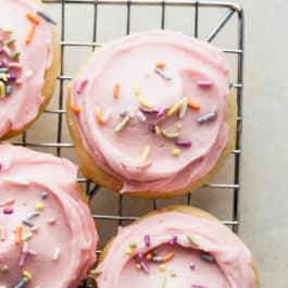 sugar cookies topped with pink buttercream and sprinkles on a cooling rack
