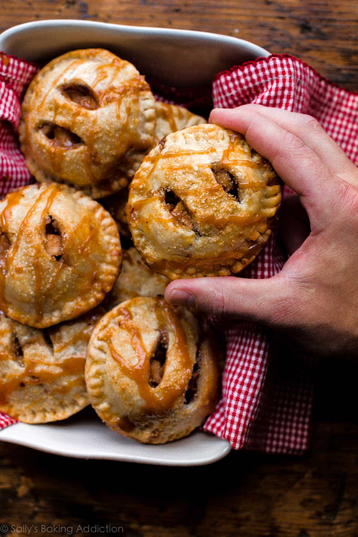 hand grabbing an apple hand pie from a baking dish