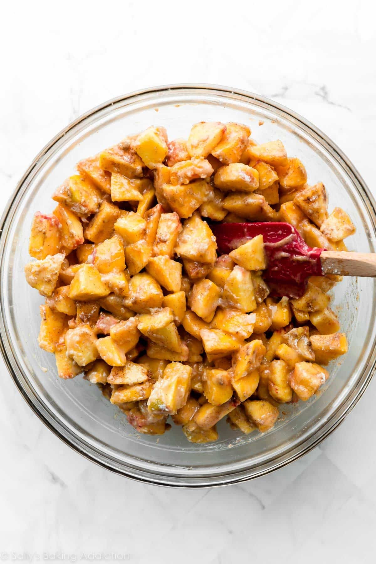 peach chunks mixed with other filling ingredients in glass bowl with red spatula.
