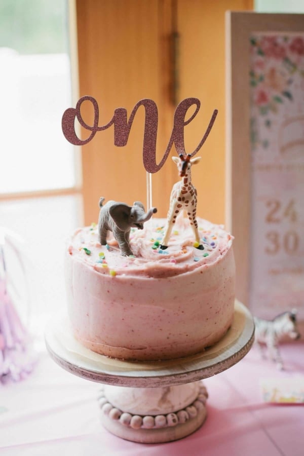 pink 1st birthday cake on a cake stand with safari animal cake toppers