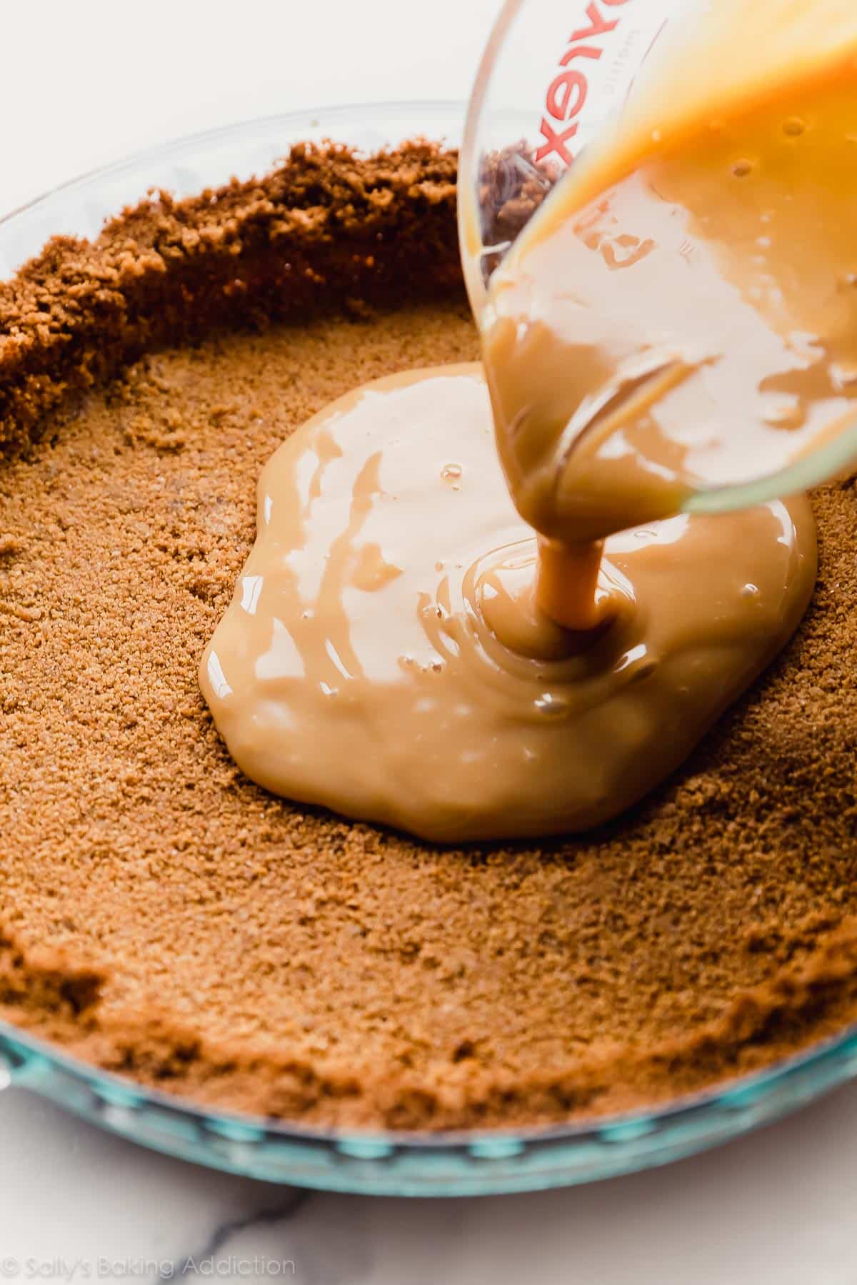 pouring dulce de leche onto graham cracker crust