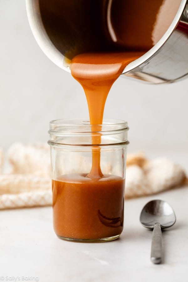pouring salted caramel sauce into a glass jar.