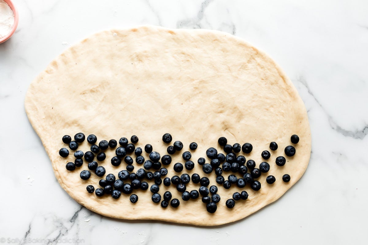 Rolled out yeast doughnut dough for blueberry fritters with blueberries on top