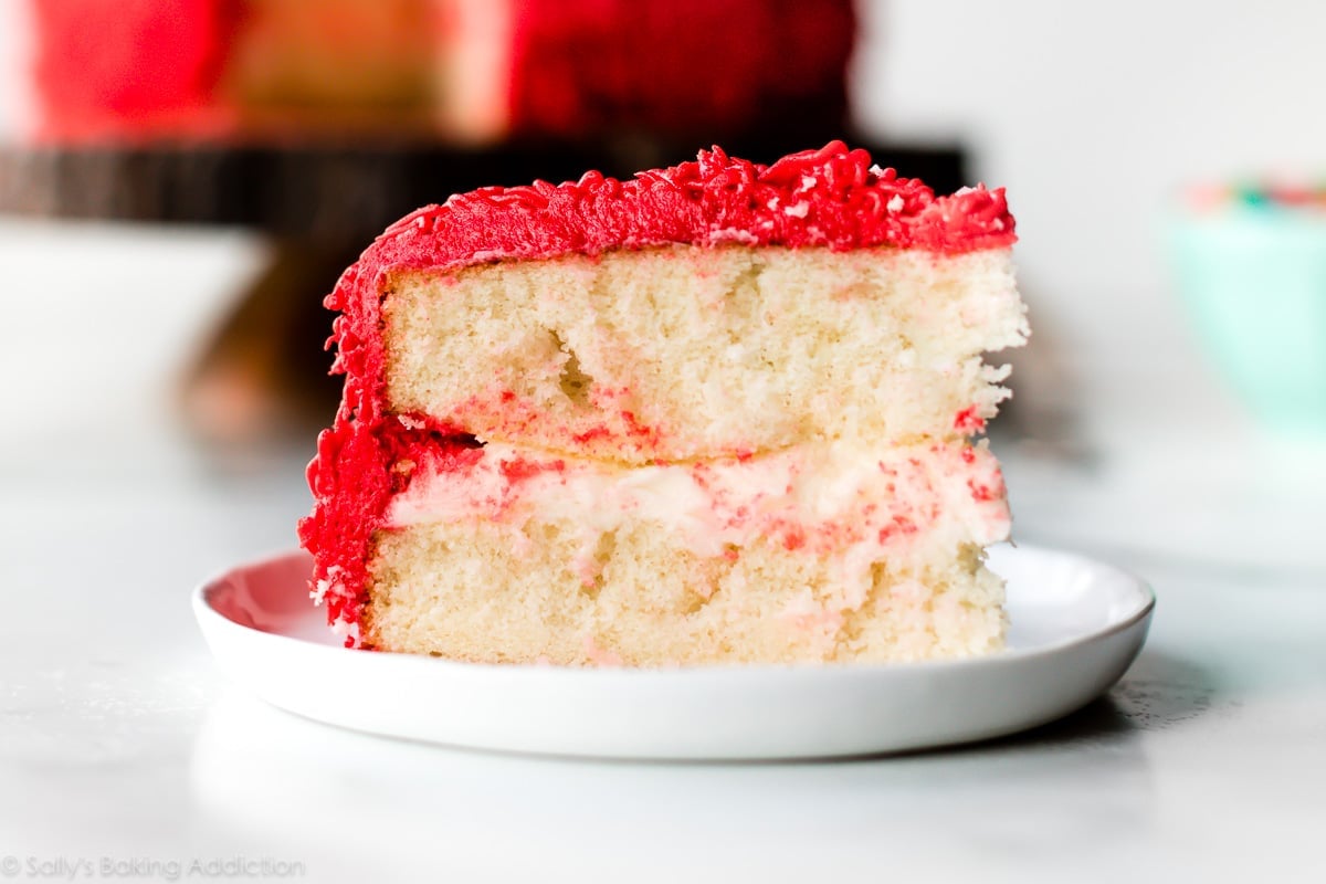 slice of white cake with red frosting on white plate
