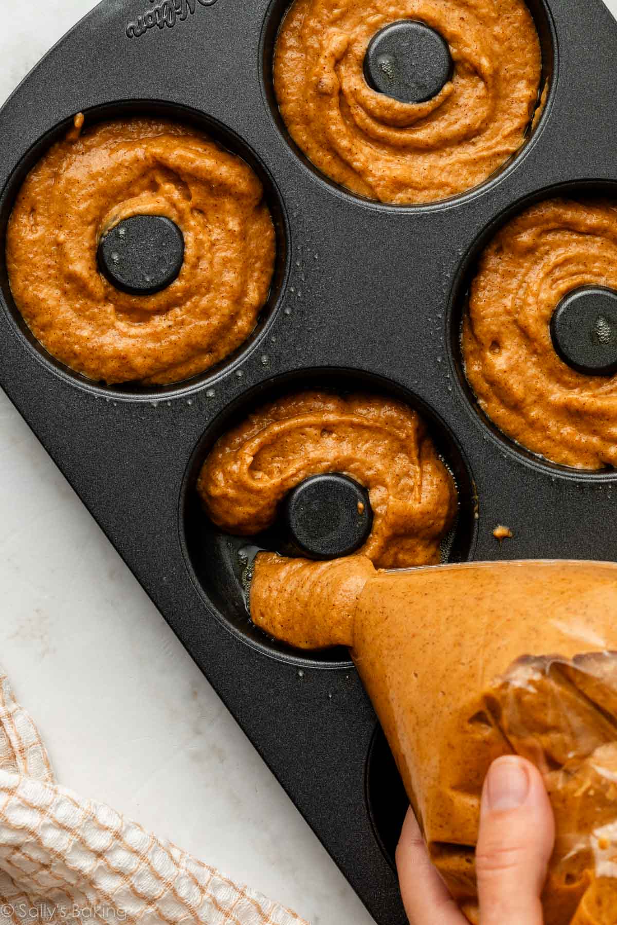 squeezing batter out of a bag into a donut pan.