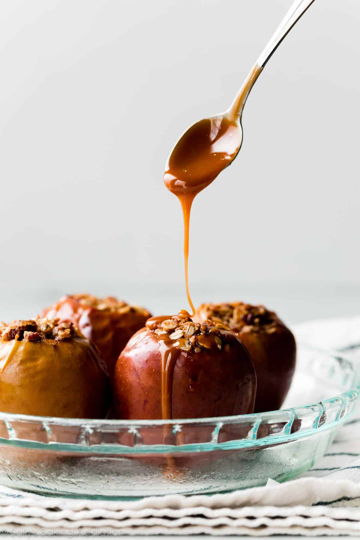 spoon drizzling caramel on baked apples