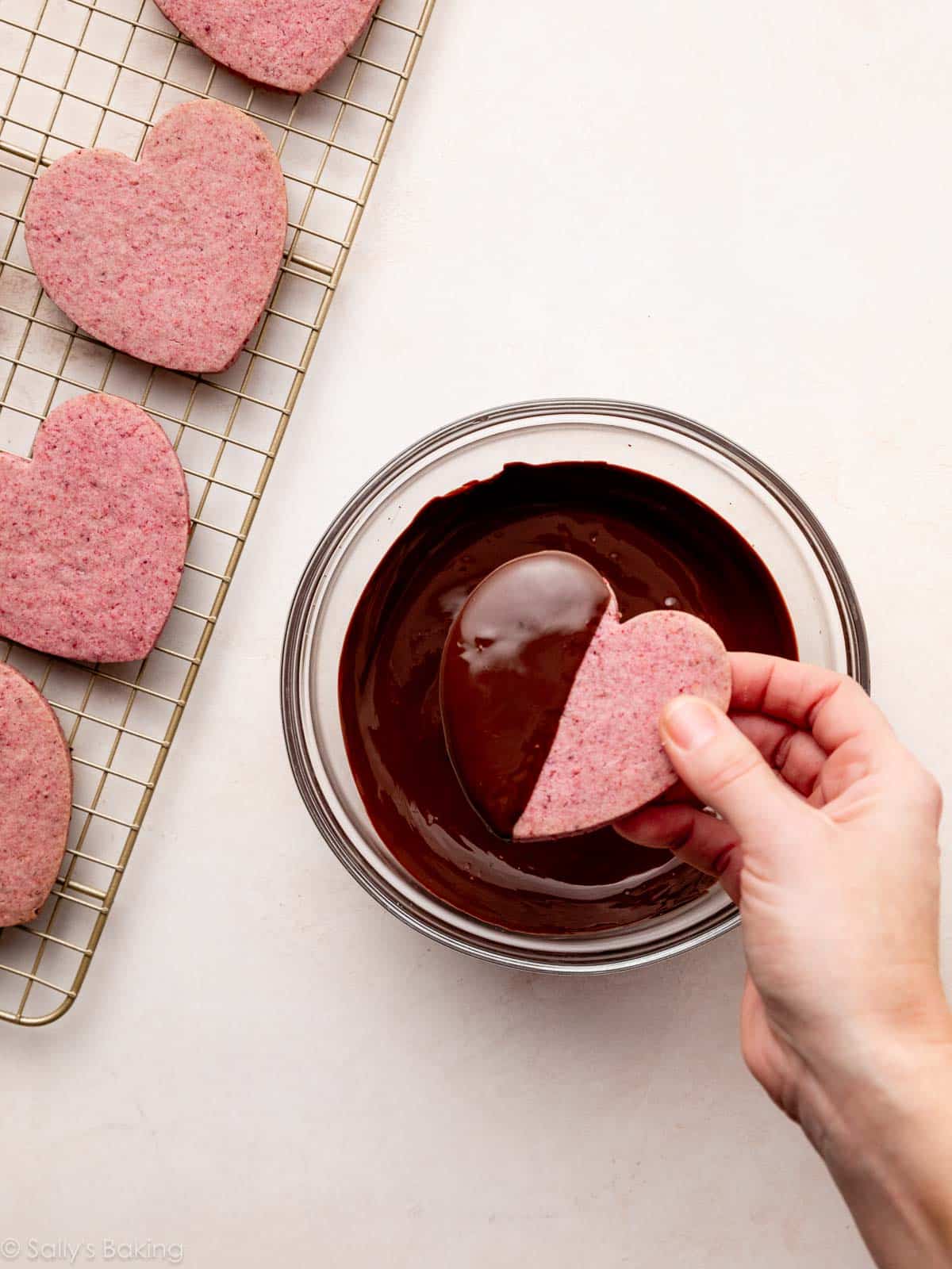hand dipping heart shaped cookie in melted chocolate.