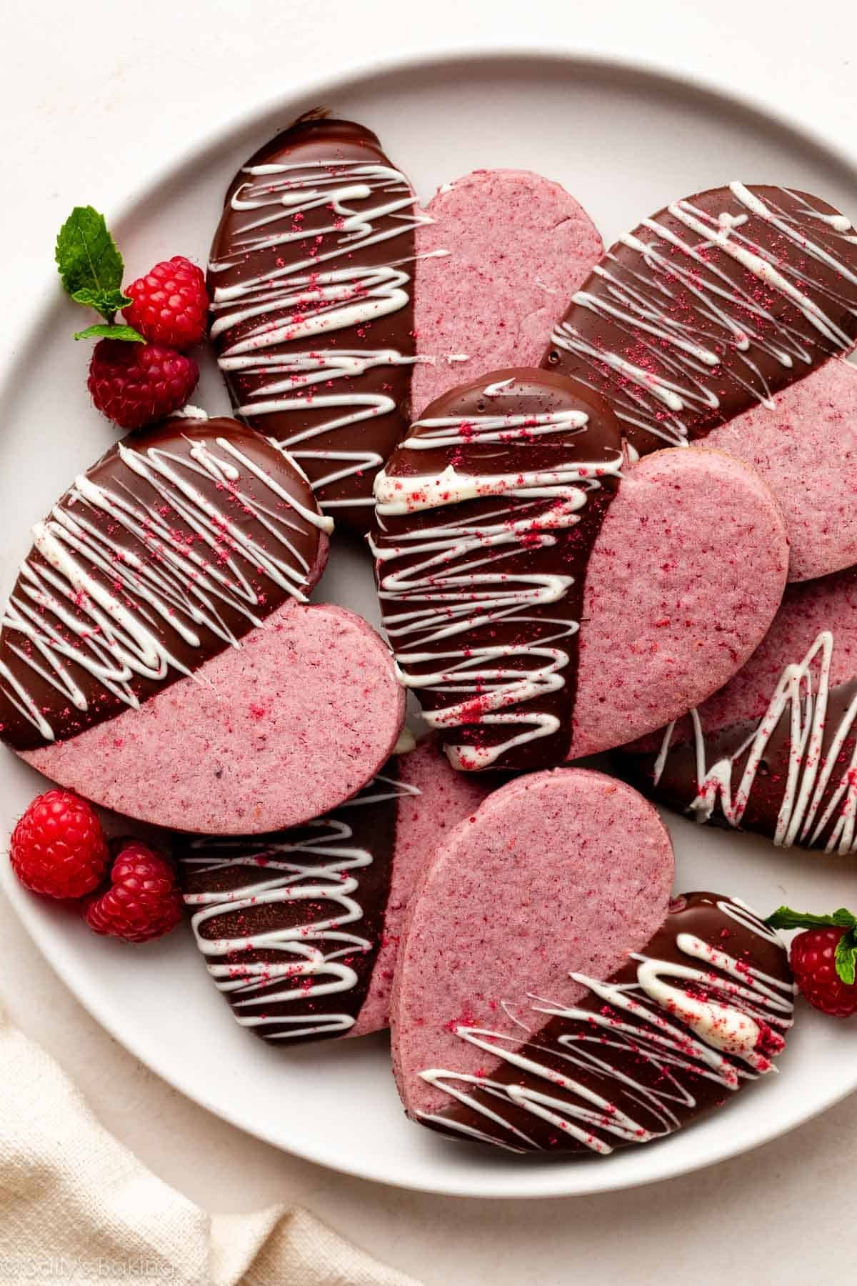 heart-shaped raspberry sugar cookies dipped in chocolate and white chocolate on white plate.