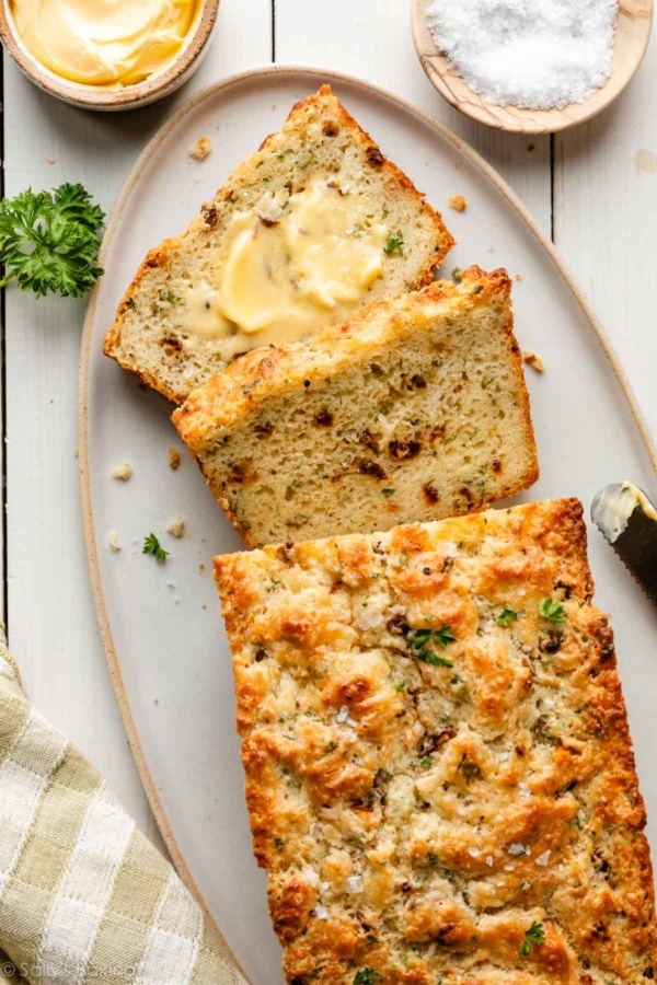 savory quick bread slices with butter, sun-dried tomatoes, parsley, and fresh basil.