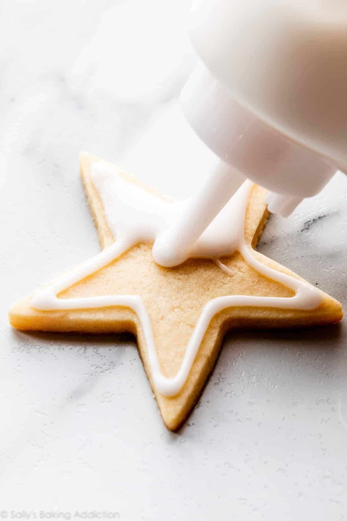 decorating a sugar cookie with white icing using a squeeze bottle