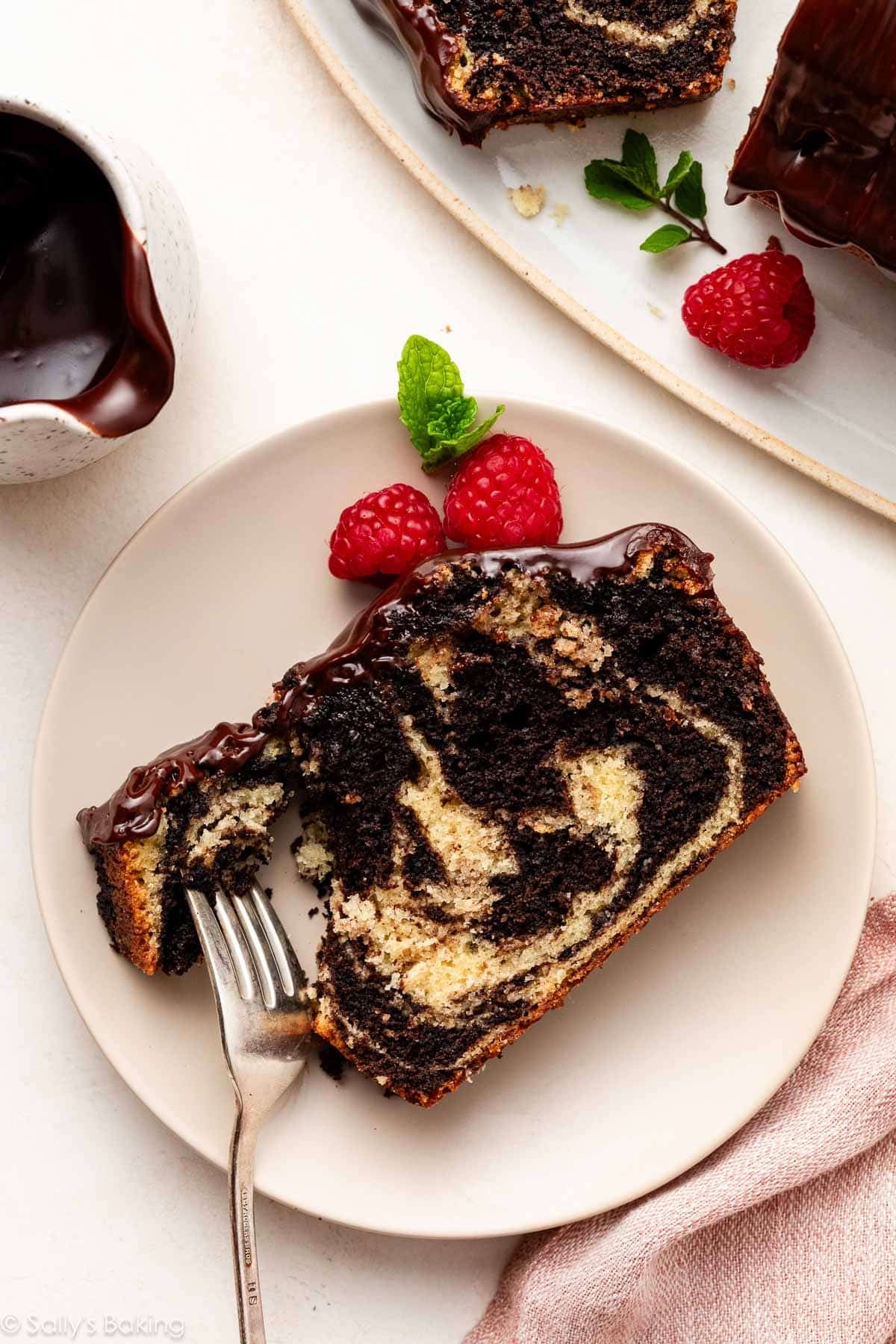slice of marble cake with ganache topping on beige plate.