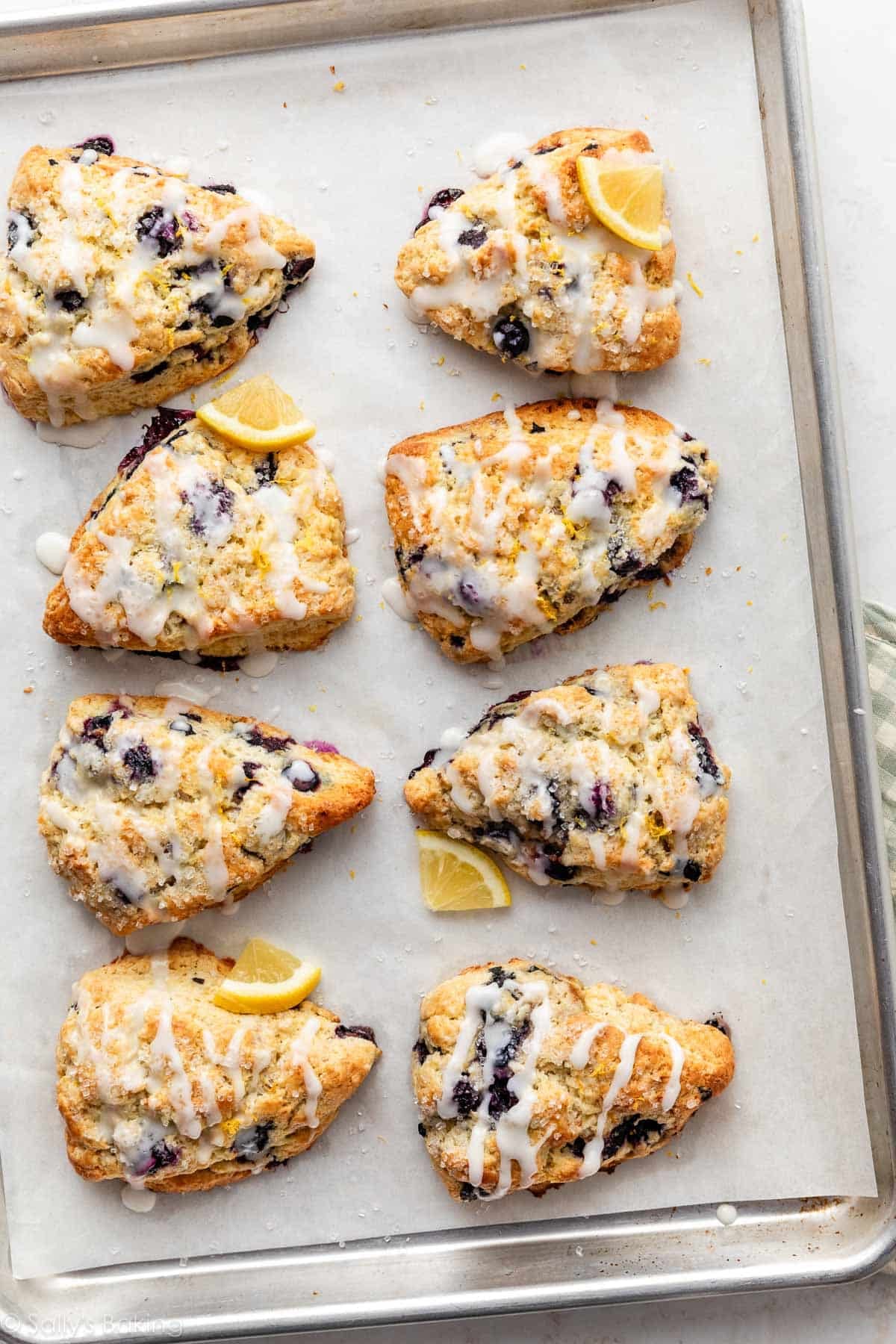 lemon blueberry scones with icing on parchment paper-lined baking sheet.