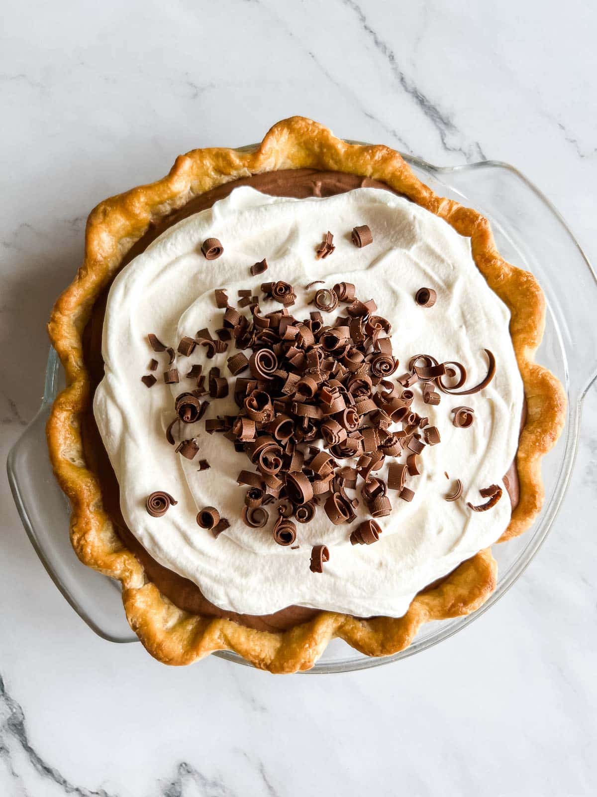 french silk pie with whipped cream and chocolate curls on top.