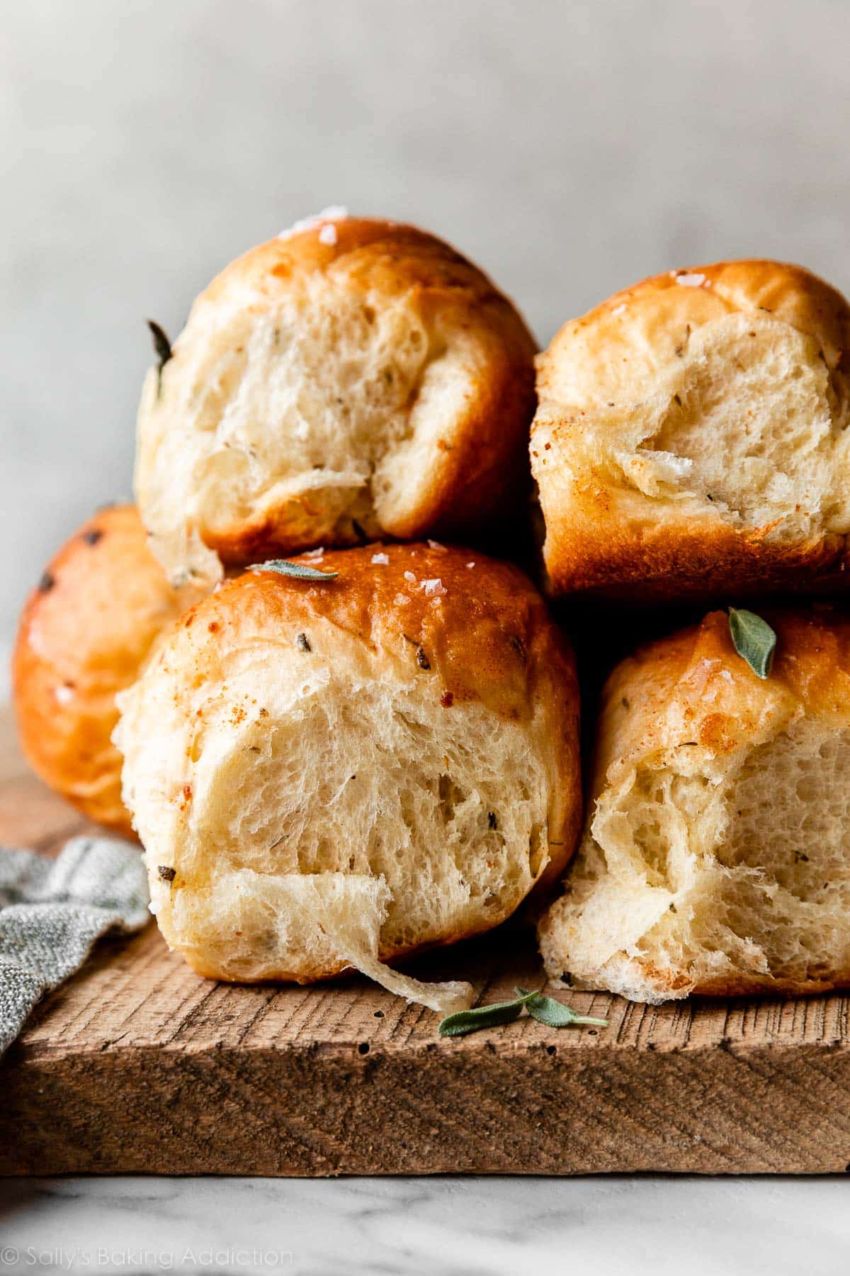 brown butter sage dinner rolls stacked together on wooden cutting board.