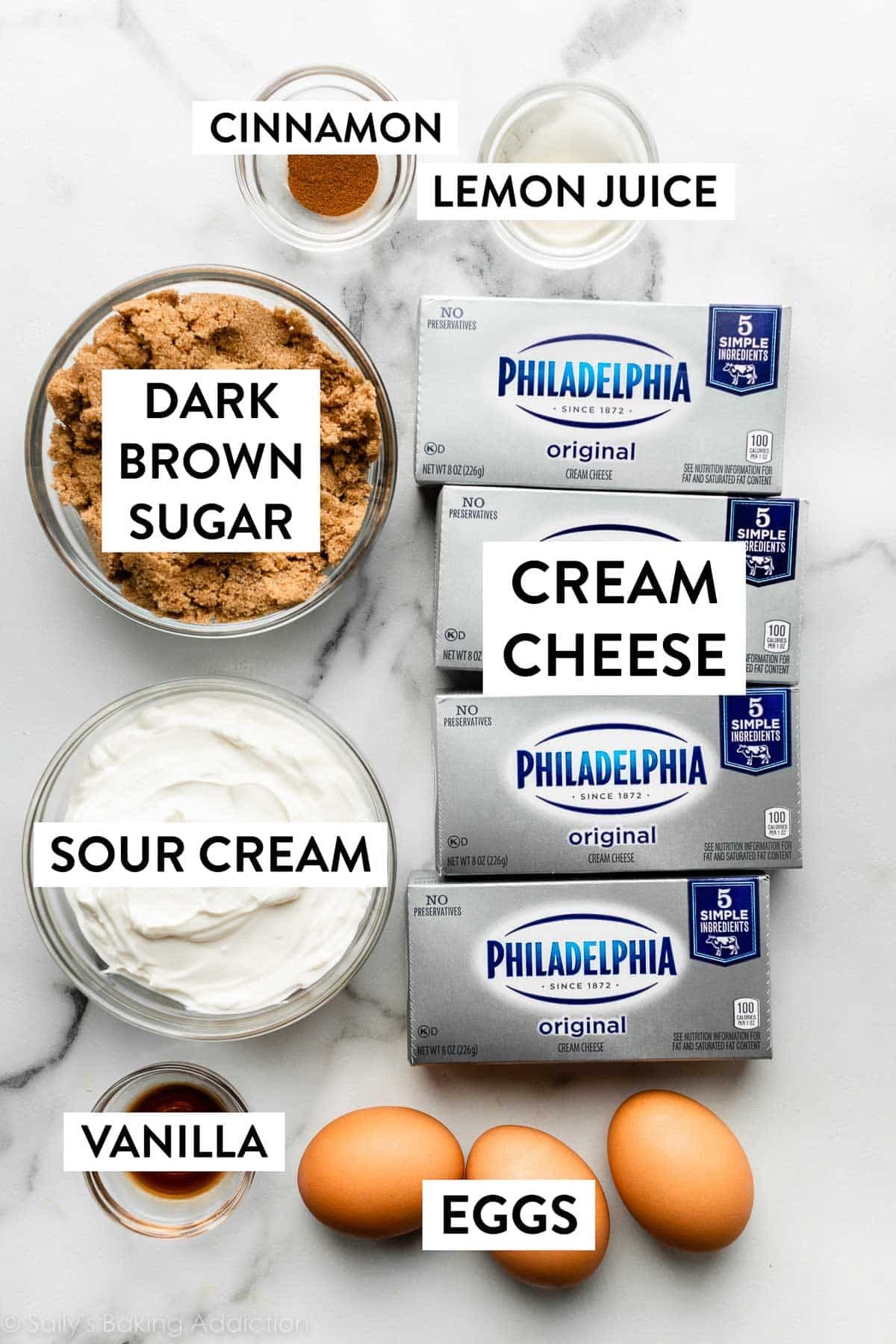 sour cream, cream cheese, vanilla, eggs, brown sugar, cinnamon, and lemon juice ingredients on marble countertop.