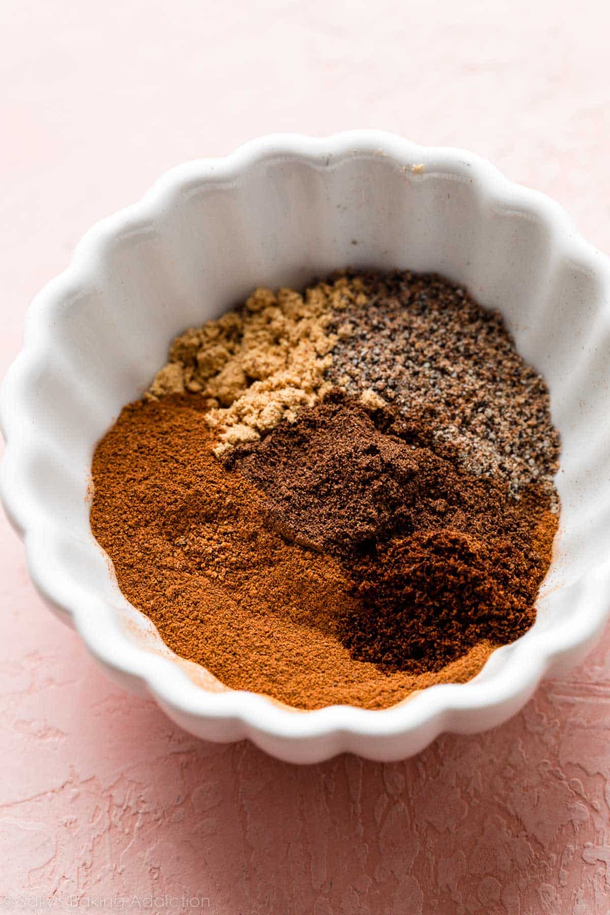 white ramekin bowl of mixed spices on pink backdrop.