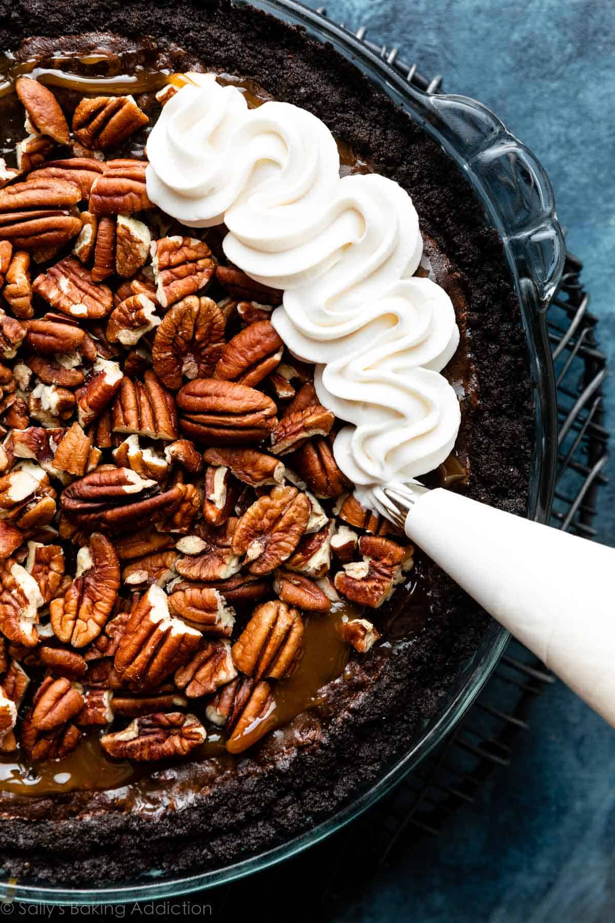 piping whipped cream on top of pecan-topped pie.