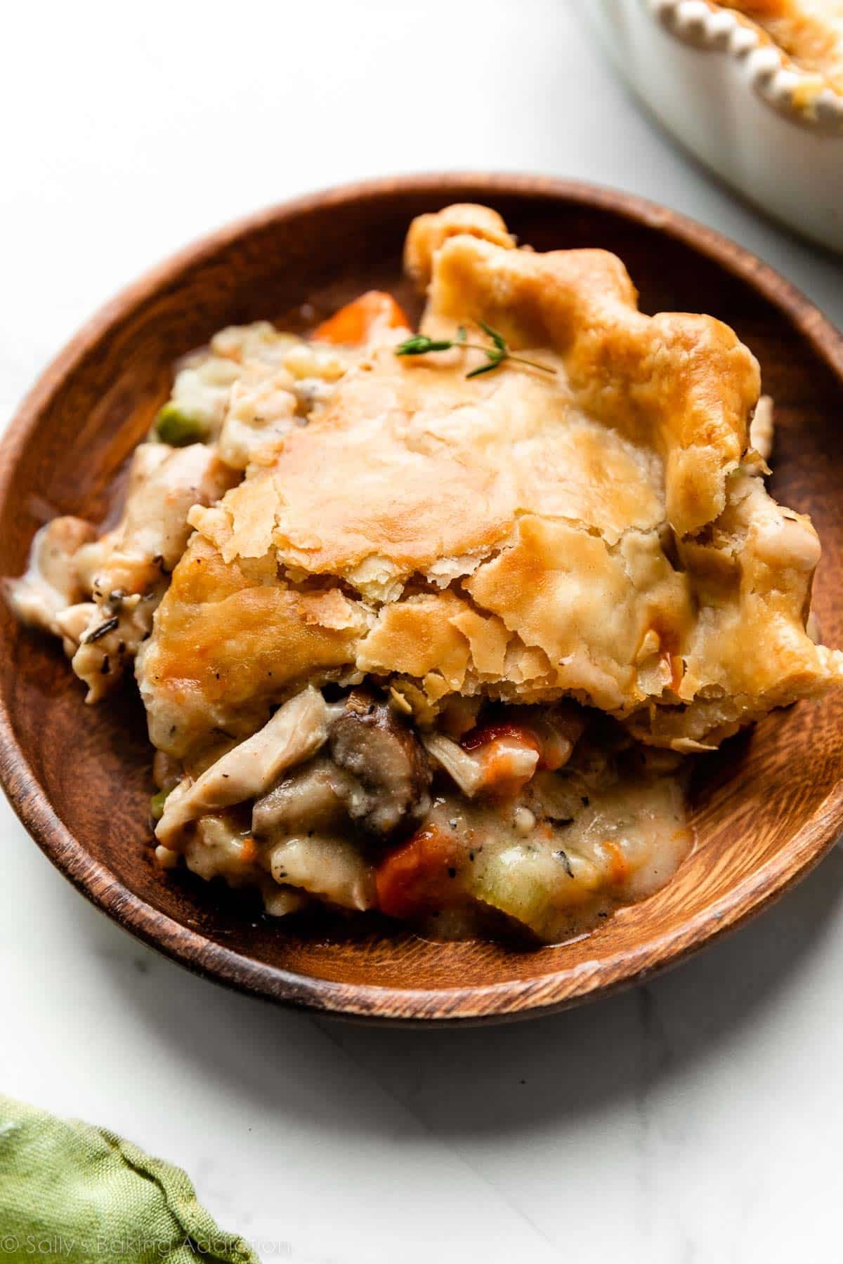 slice of turkey pot pie with golden flaky pie crust on brown wooden plate.