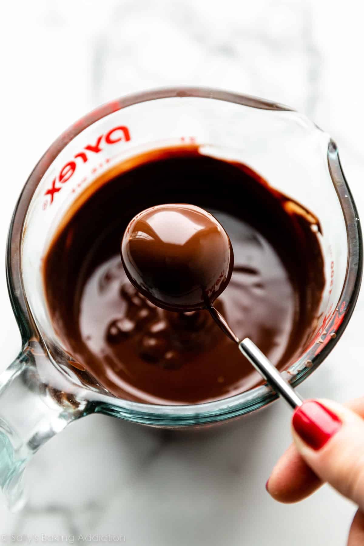 hand holding dipping tool with chocolate covered truffle on it.